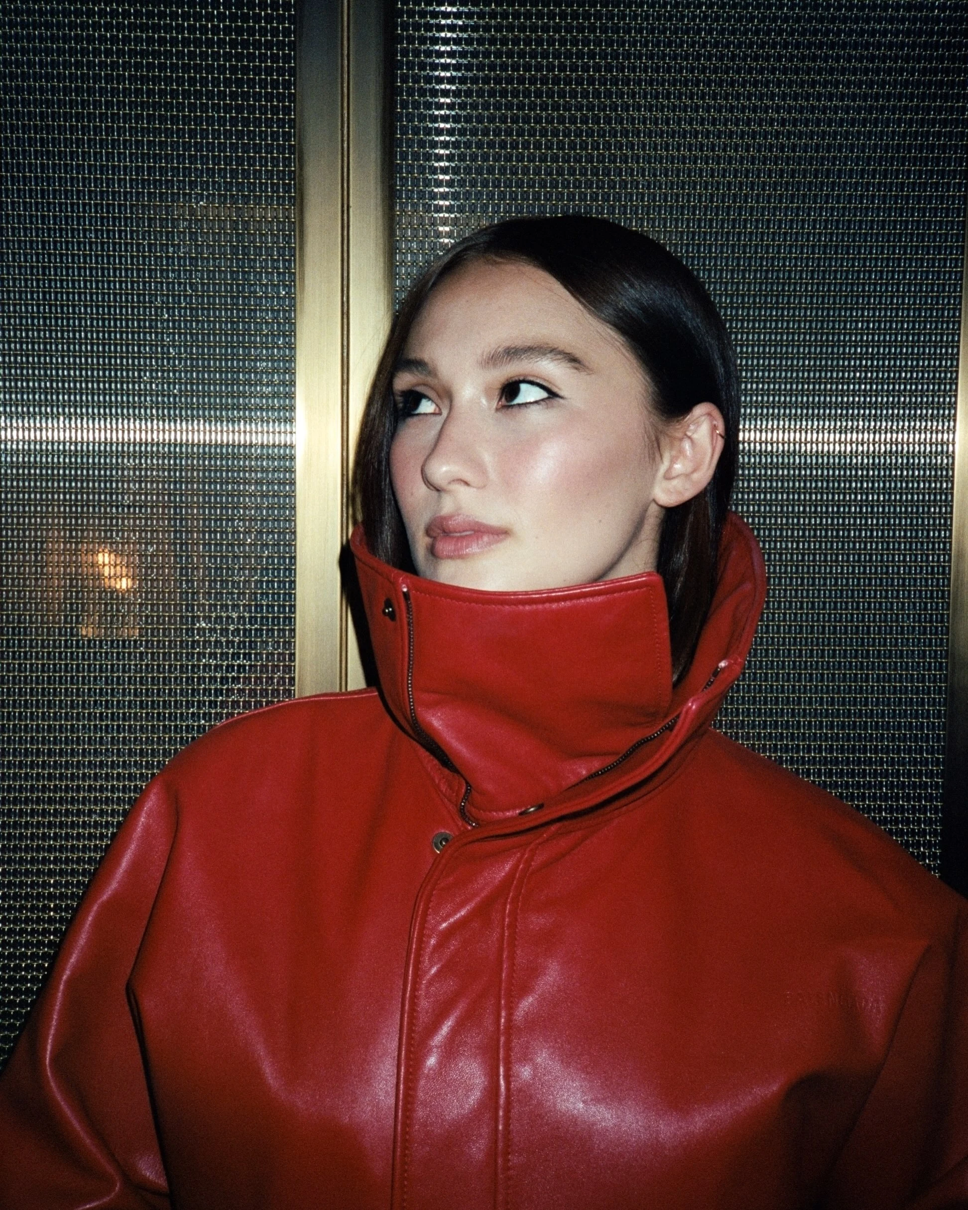 Glossy red leather bomber with an oversized high collar, black crew-neck top, and dark straight-leg jeans.