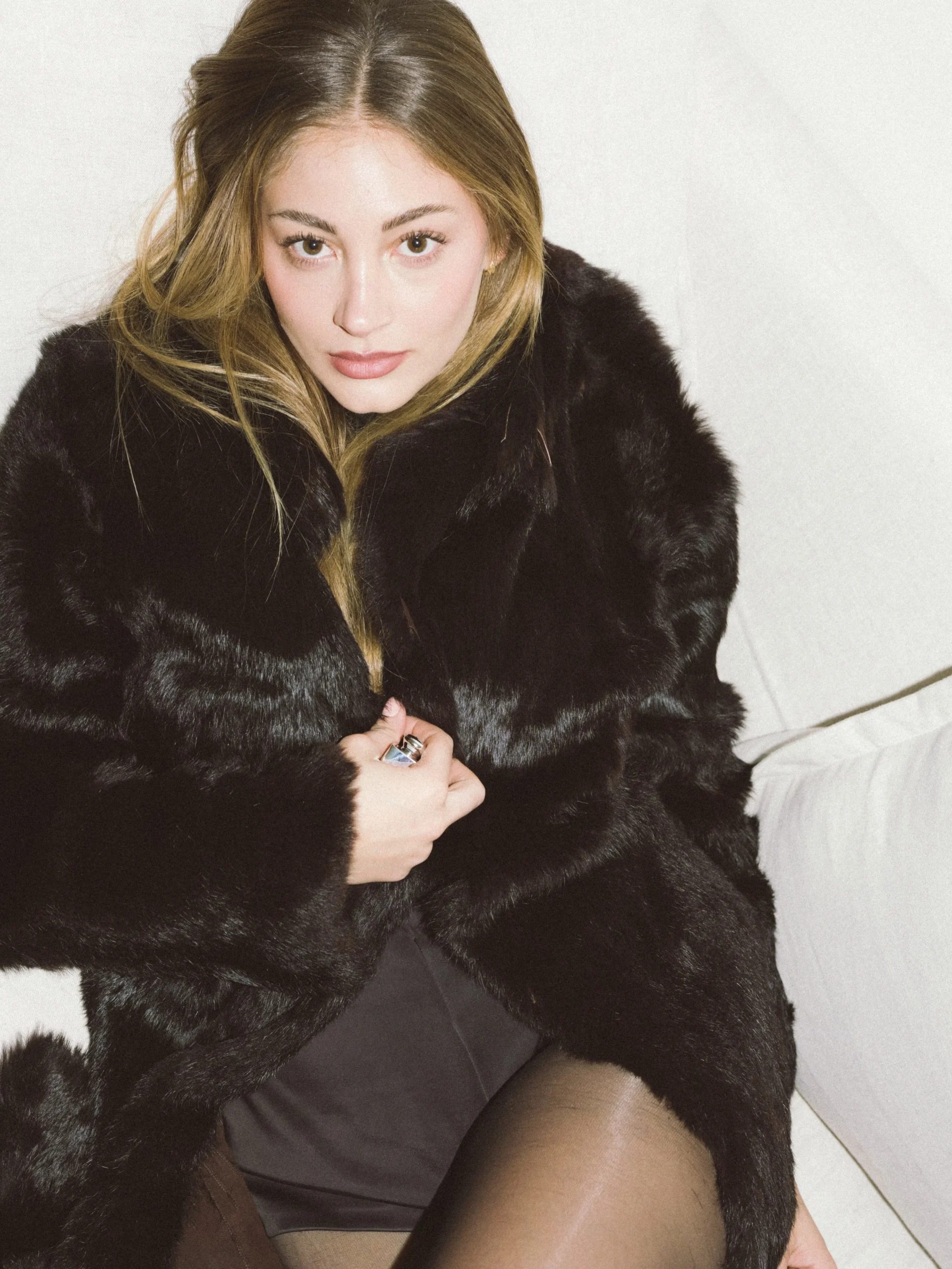 Oversized black faux-fur coat open over a dark mini dress and sheer black tights.