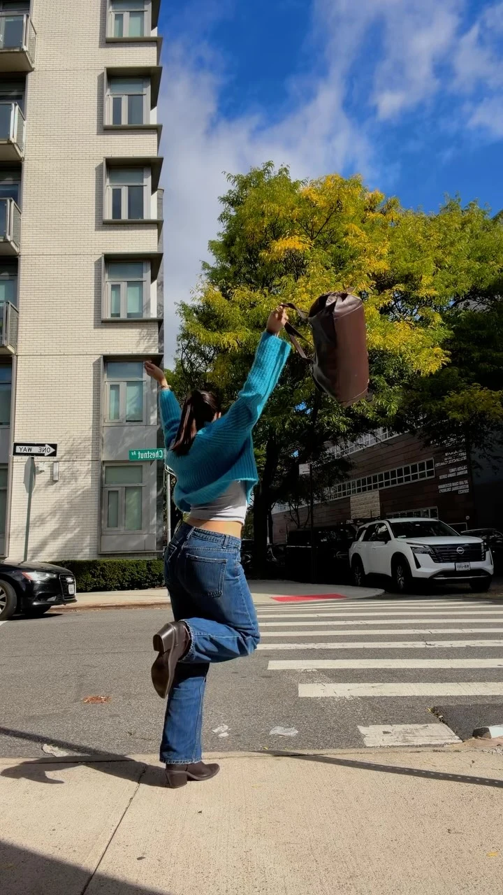 Person in teal top, blue straight-leg jeans, and brown ankle boots on a city sidewalk.
