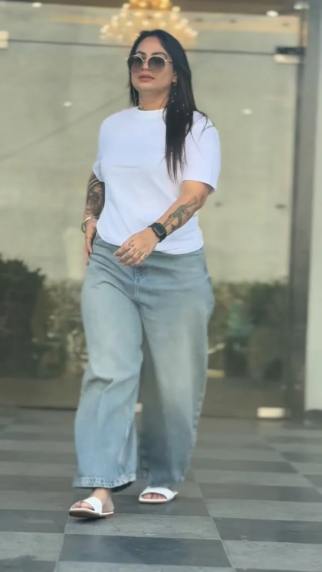 Oversized white tee tucked into light-wash wide-leg baggy jeans with white slide sandals.