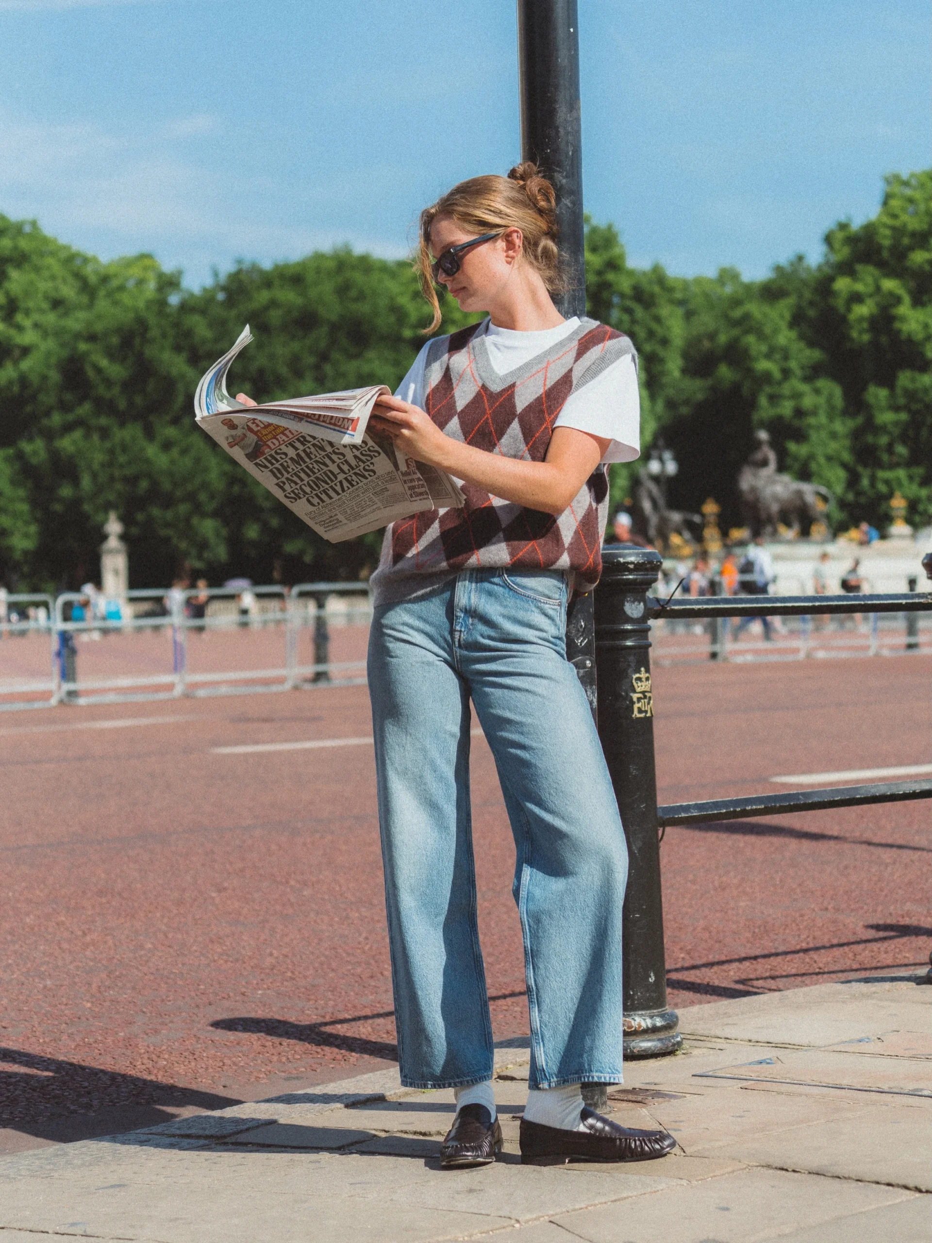 Grey-brown argyle sweater vest over white tee, wide-leg jeans, loafers, and sunglasses.