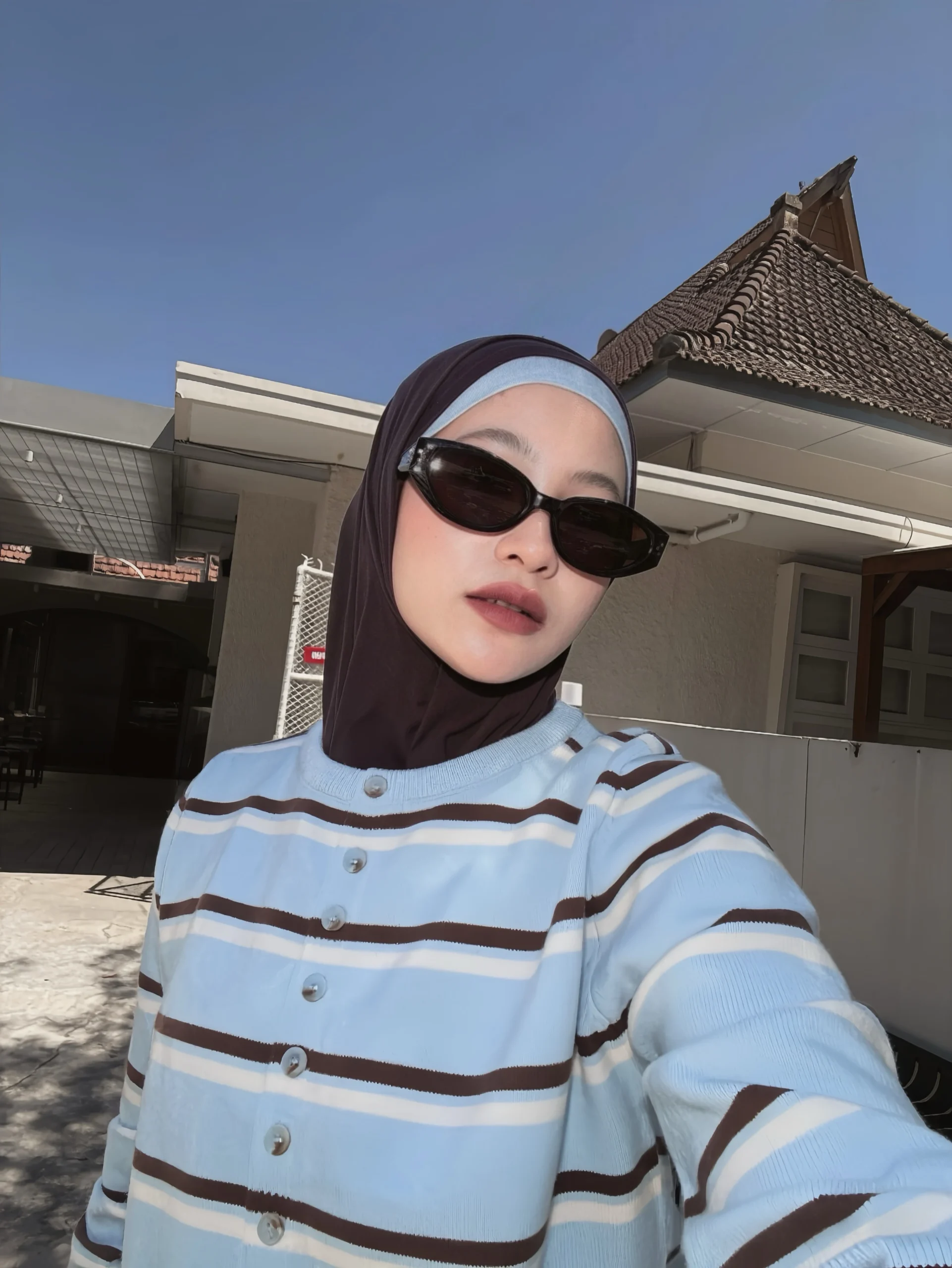 Baby-blue striped knit cardigan styled with white wide-leg trousers, dark hijab, and small handbag.