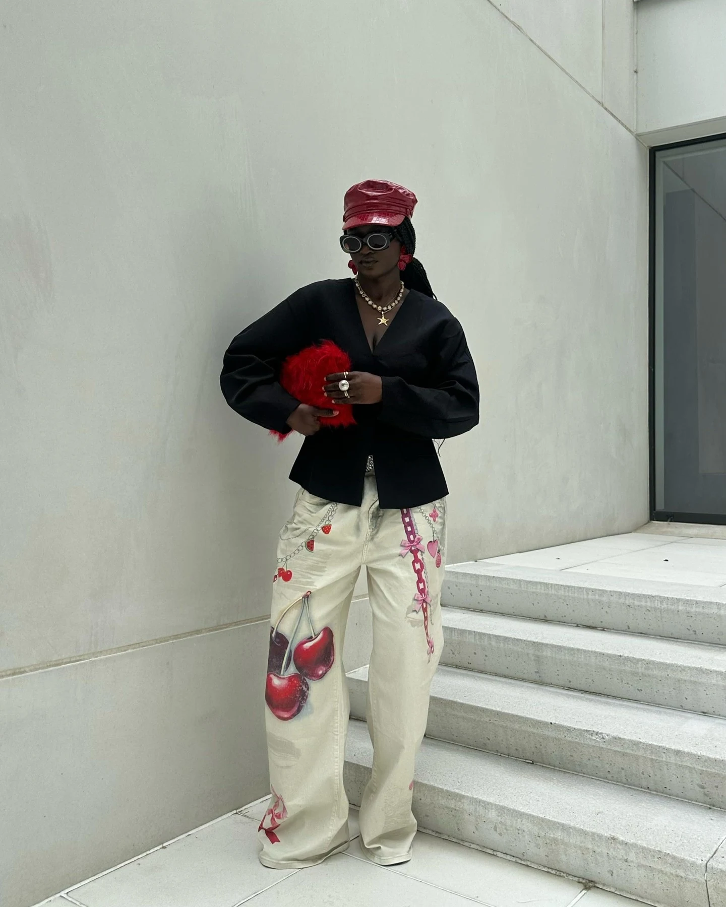 Black blazer and cream cherry-print wide-leg trousers styled with a glossy red head covering.