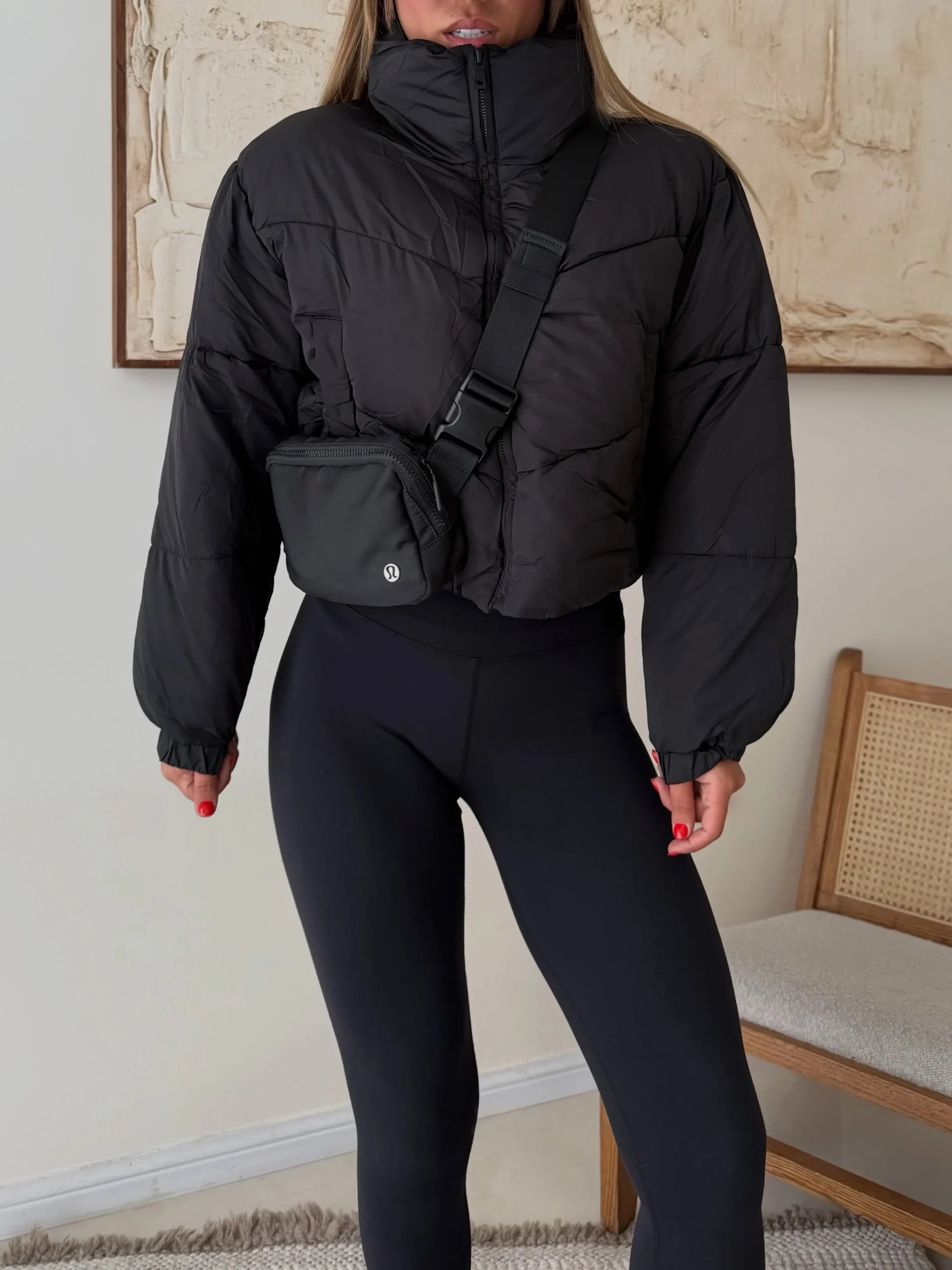 Black cropped puffer jacket with high collar worn over fitted black leggings with a crossbody bag.