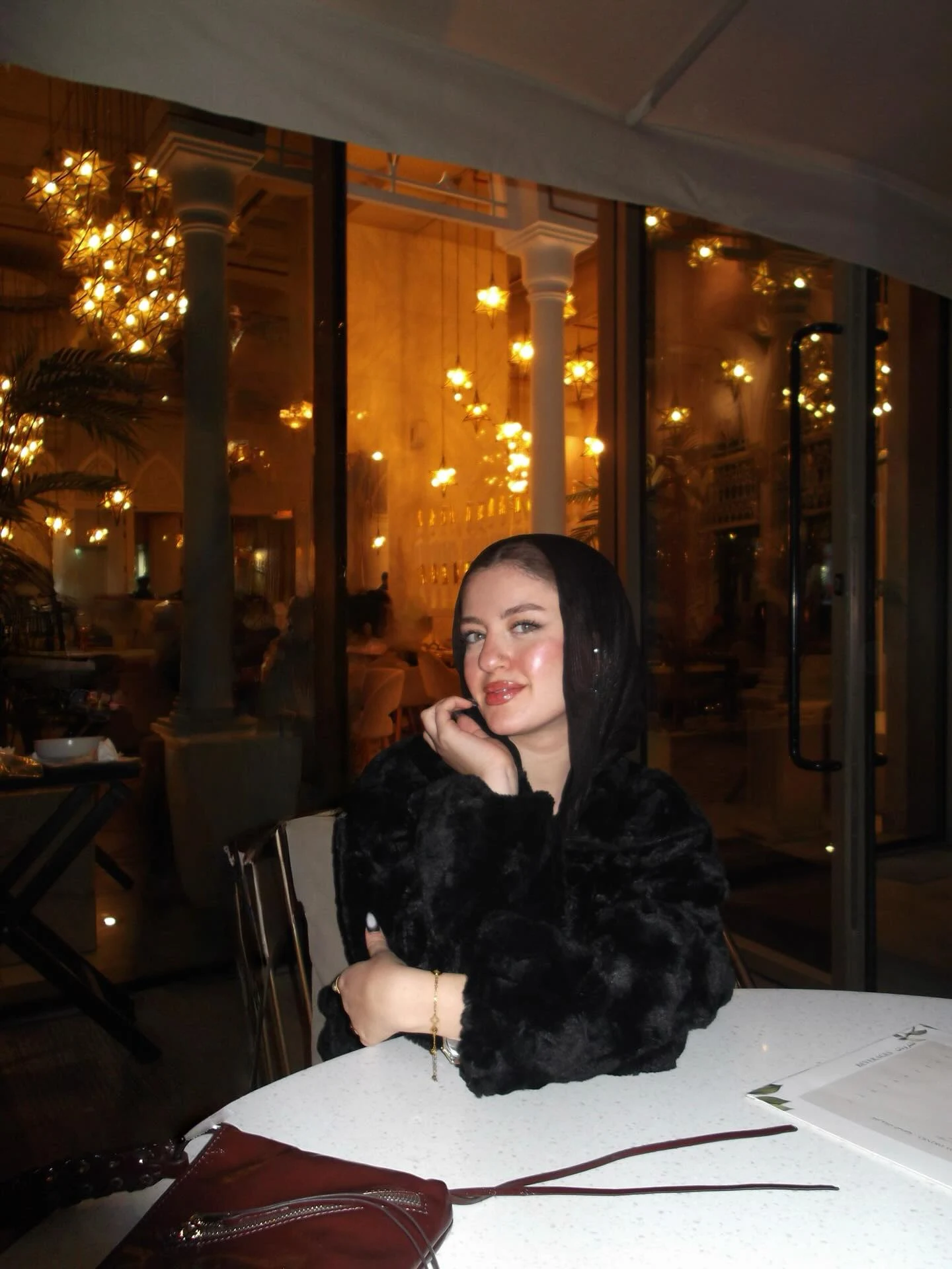 Woman wearing a black faux-fur hooded coat with a black head covering.