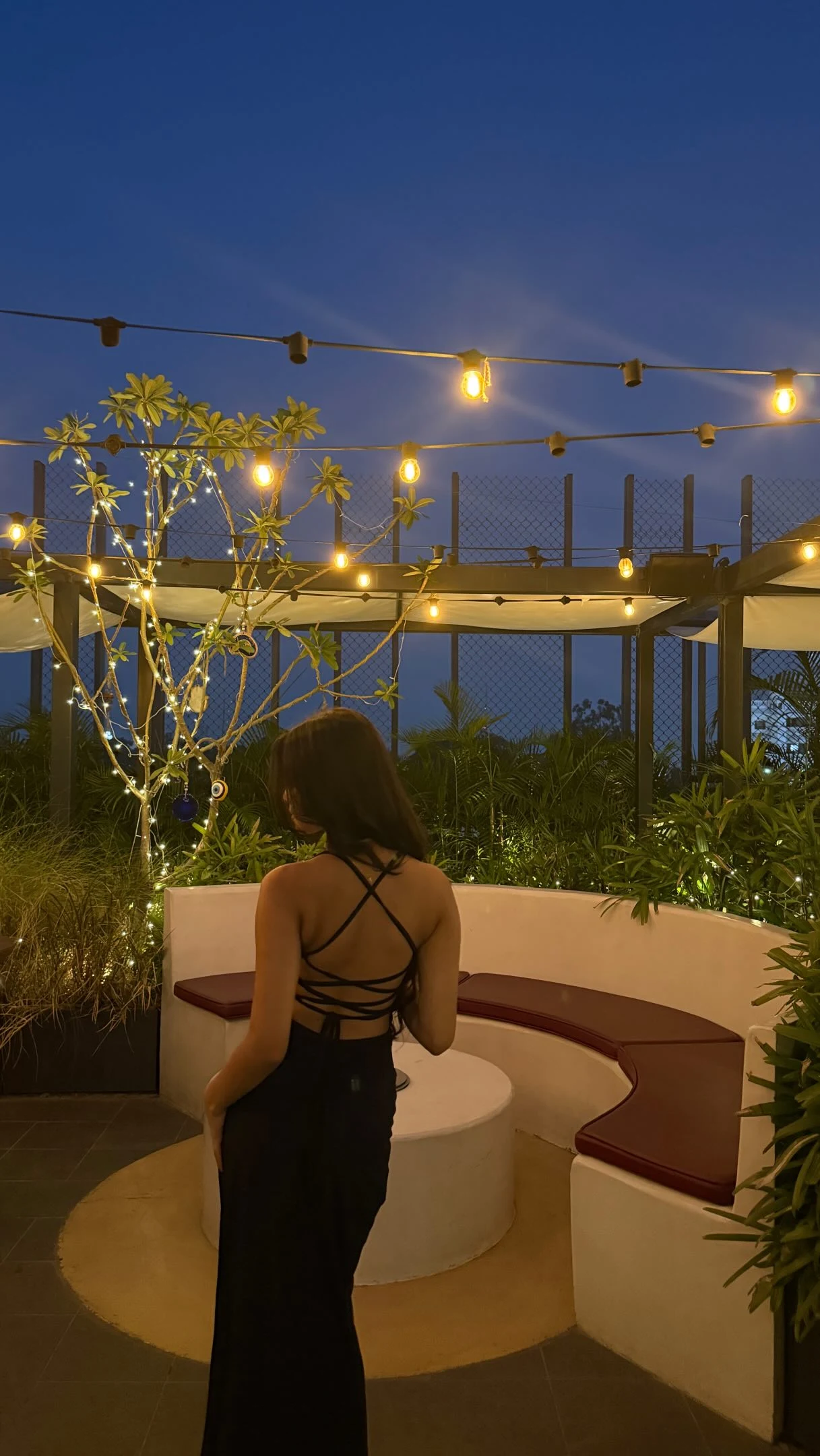 Woman in a crisscross strappy black top and floor-length black skirt photographed from behind at night.