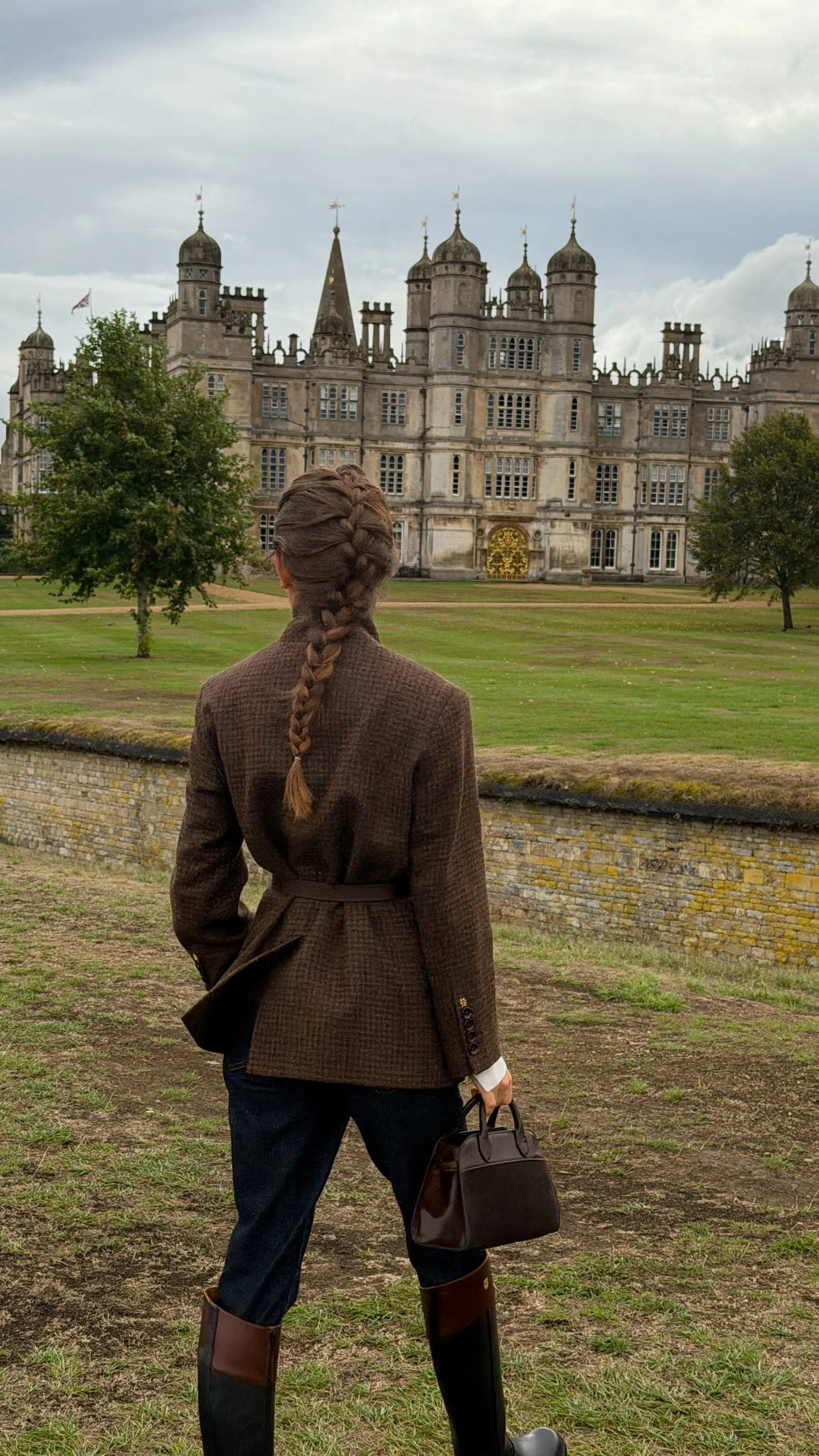 Woman wearing a brown tweed blazer, white shirt, dark jeans, and tall brown riding boots.
