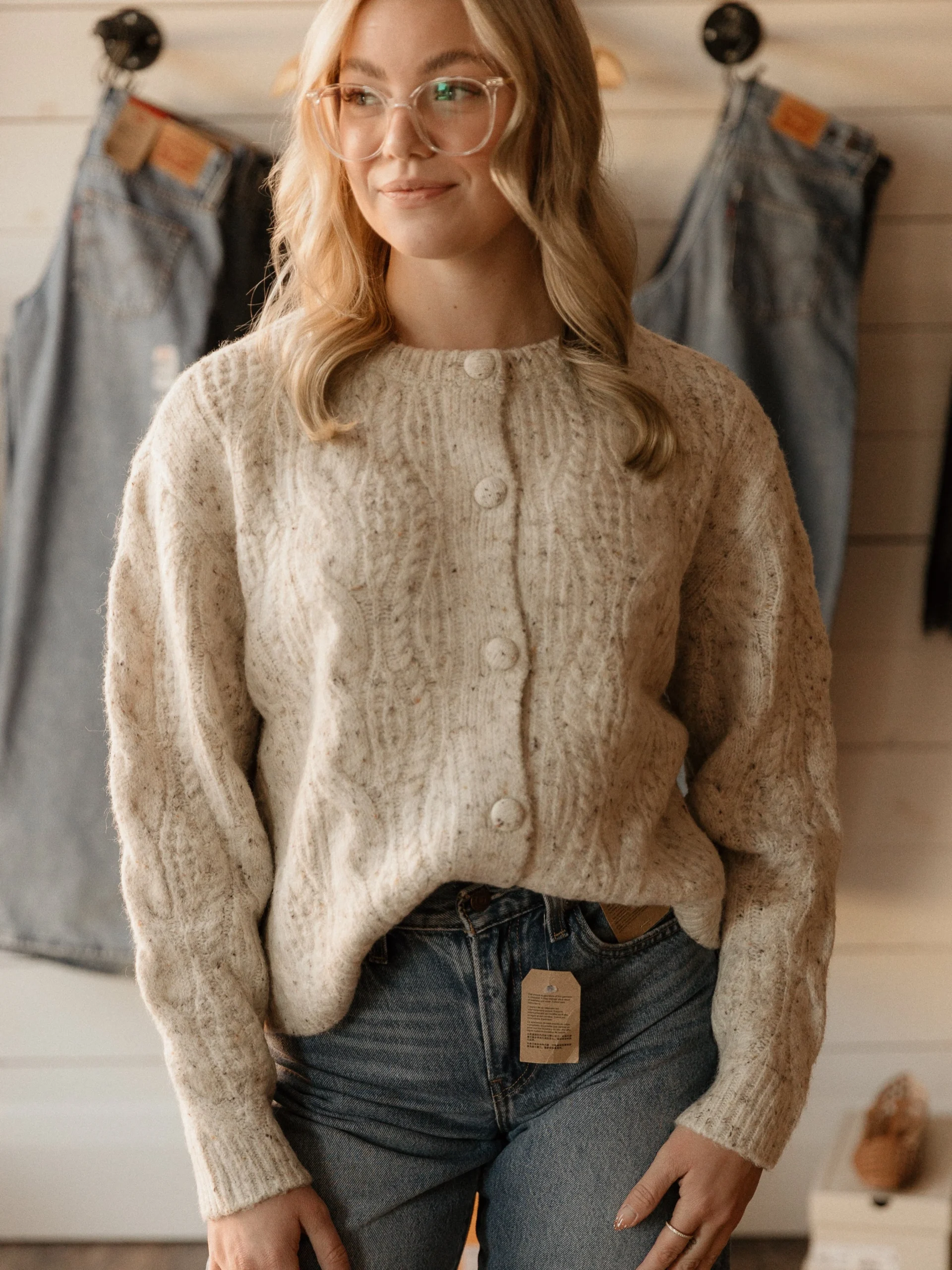 Cream speckled cable-knit cardigan with large buttons and high-waisted blue denim jeans.