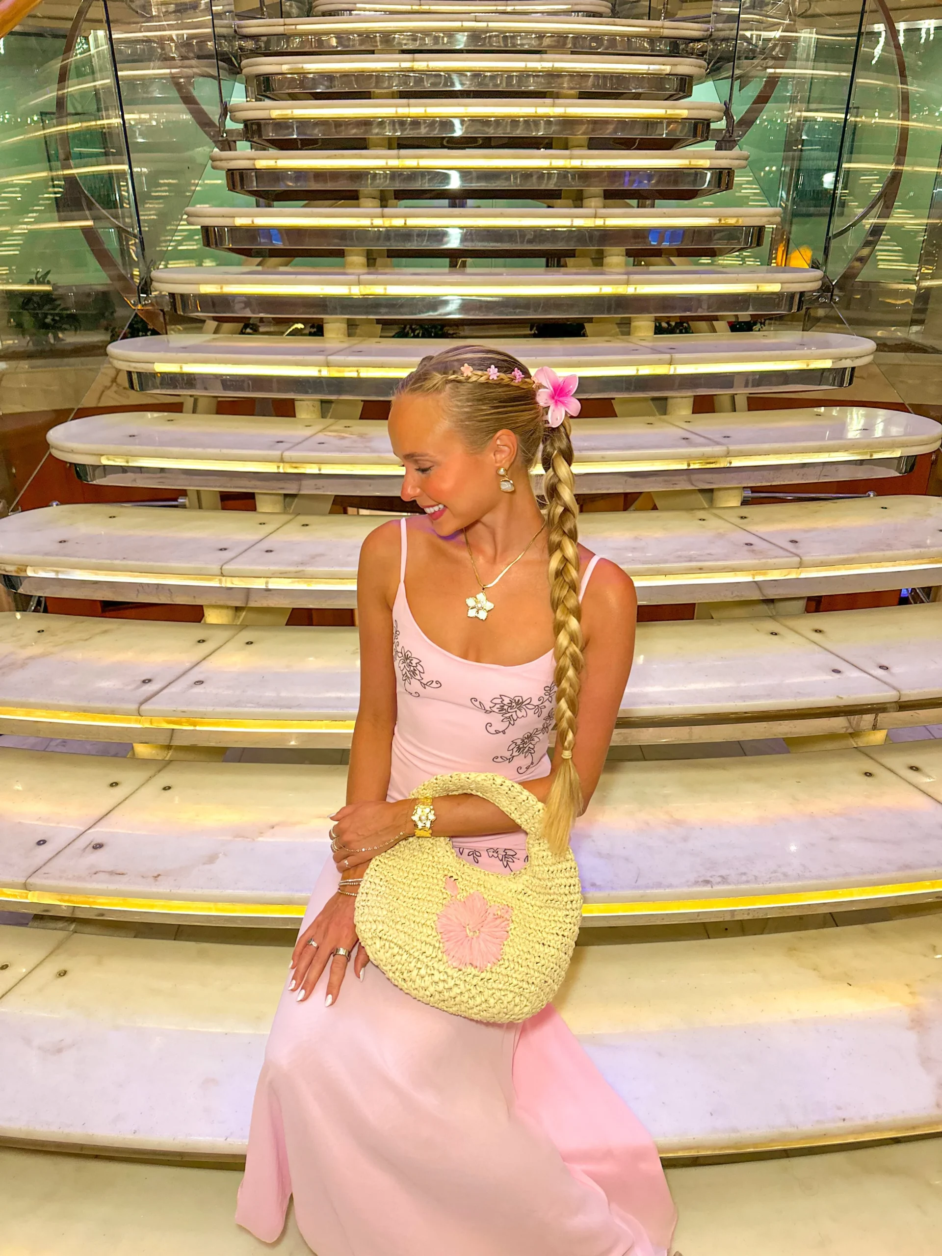Woman wearing a light pink floral embroidered maxi dress carrying a cream crochet handbag.