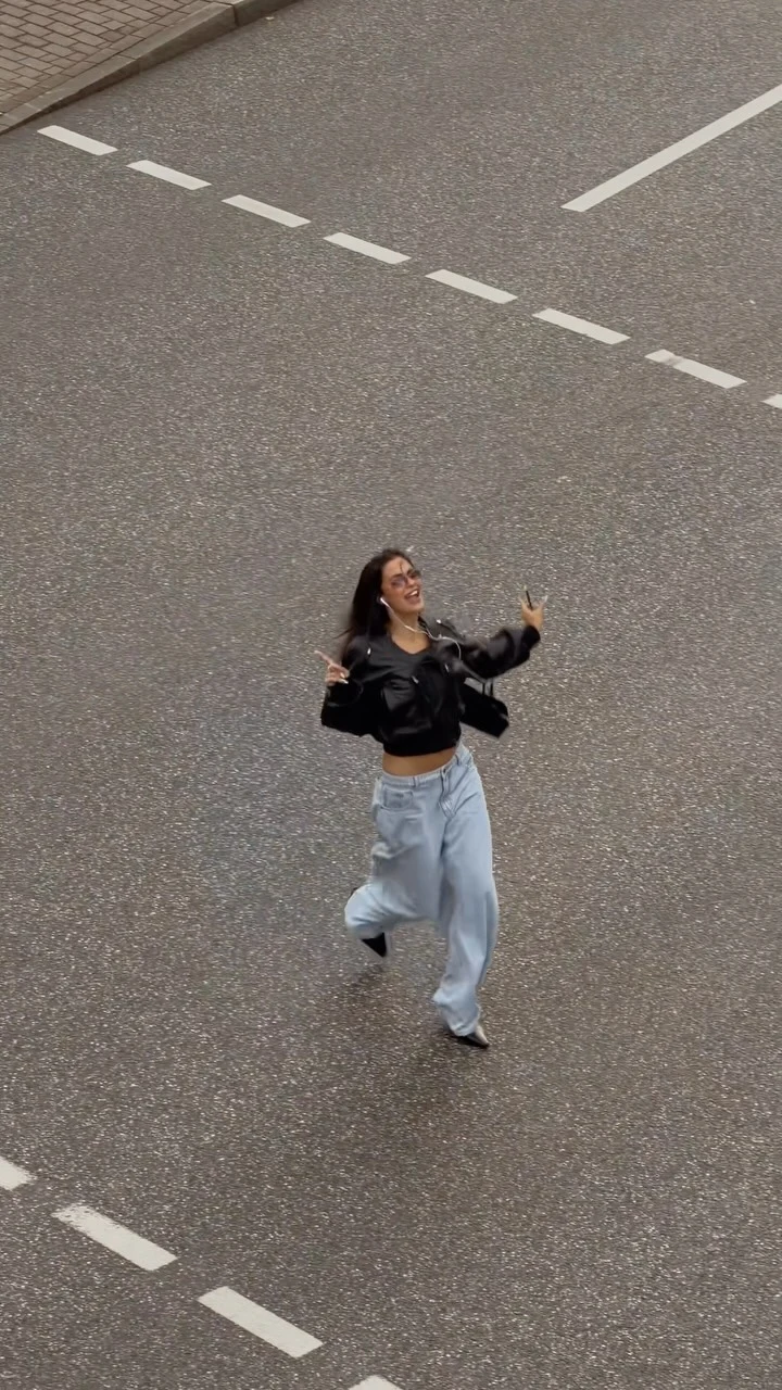 Woman wearing light-wash baggy jeans, a black cropped zip-up jacket, and a small black bag.