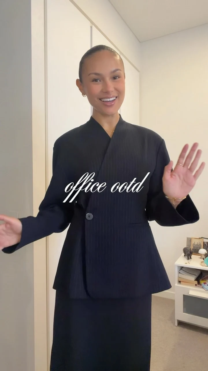 Woman wearing a navy pinstripe blazer, matching maxi skirt, flat heels, and a gold watch.