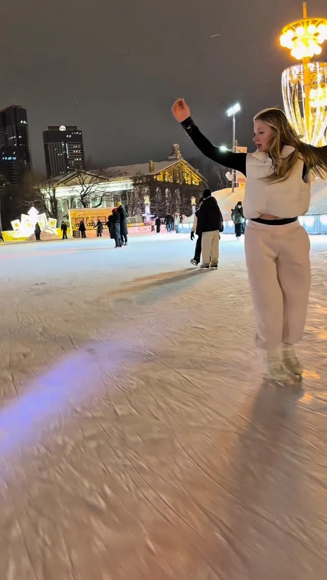 Person in white fitted top and matching pants skating at a lit outdoor rink at night.