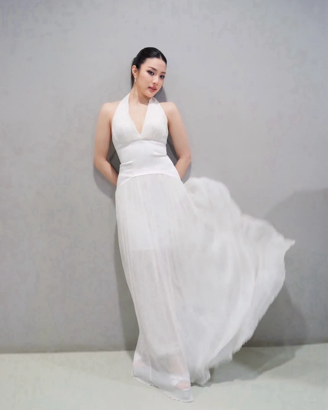 Woman wearing a white halter-neck satin evening gown with a sleek fitted silhouette.