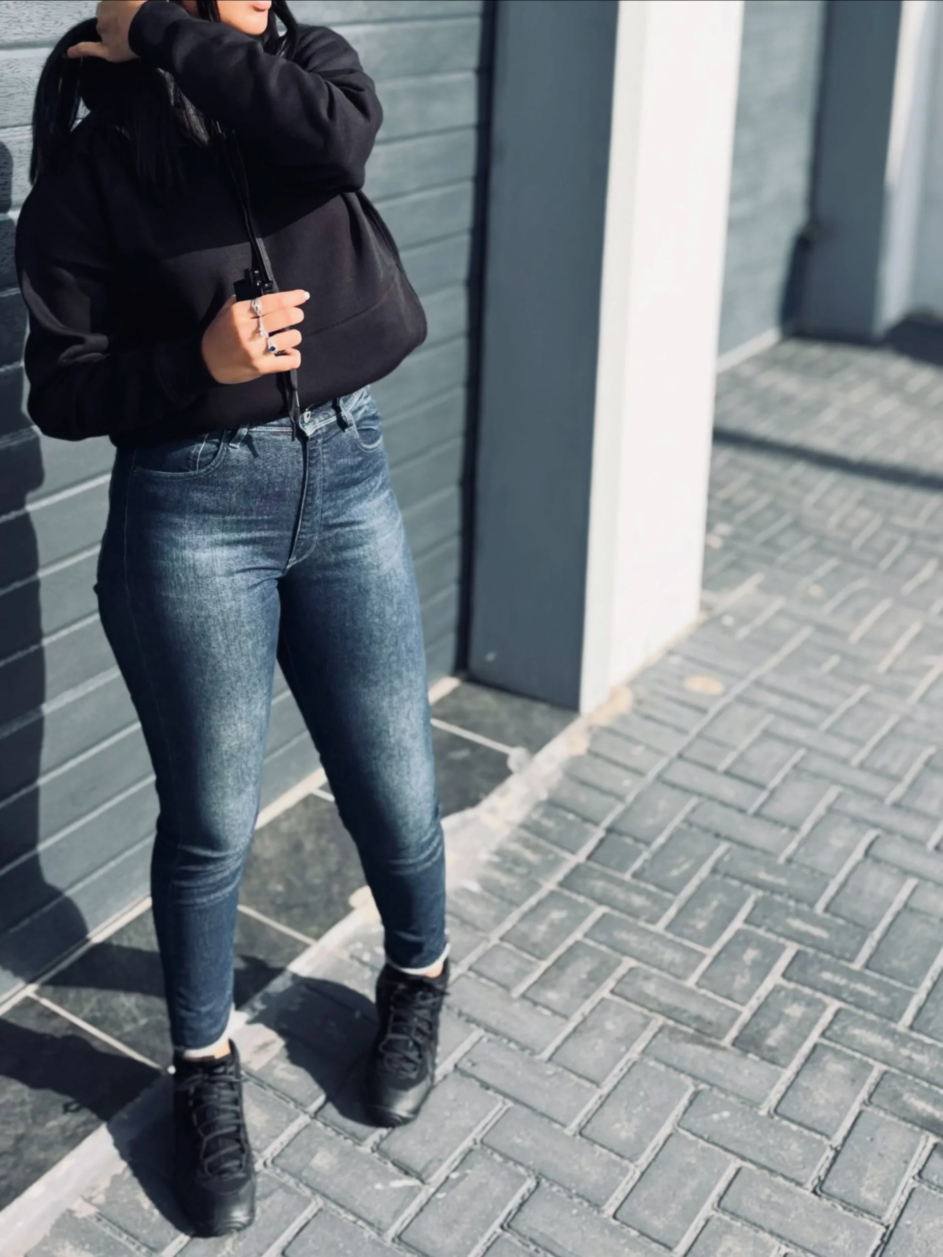 Black zip hoodie with fitted faded blue jeans cuffed above black lace-up shoes.