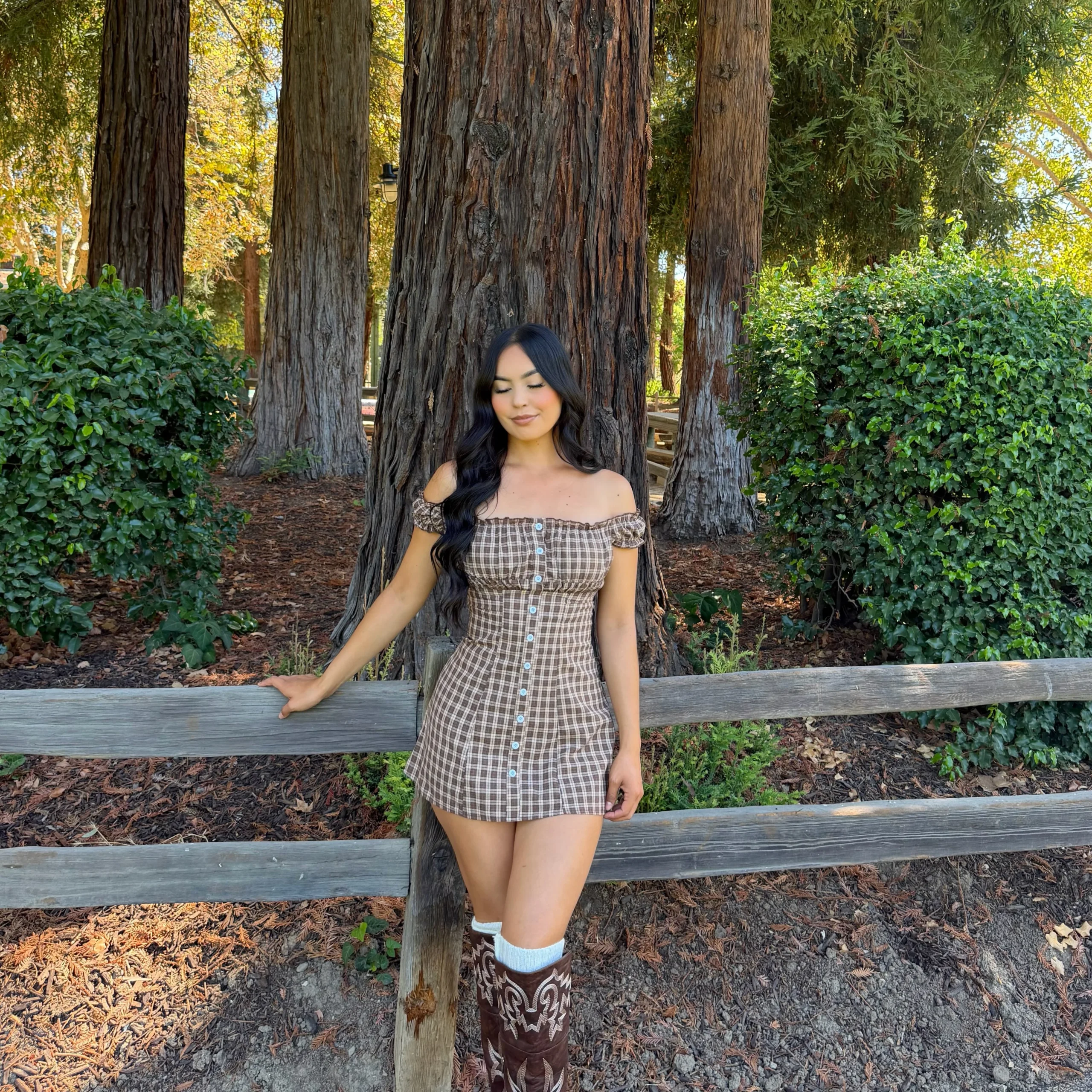 Woman wearing a brown plaid mini dress with puff sleeves and tall patterned brown boots.