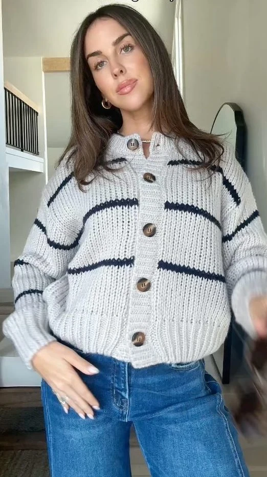 Cream black-striped cardigan with wooden buttons worn over high-rise blue barrel jeans and oval sunglasses.