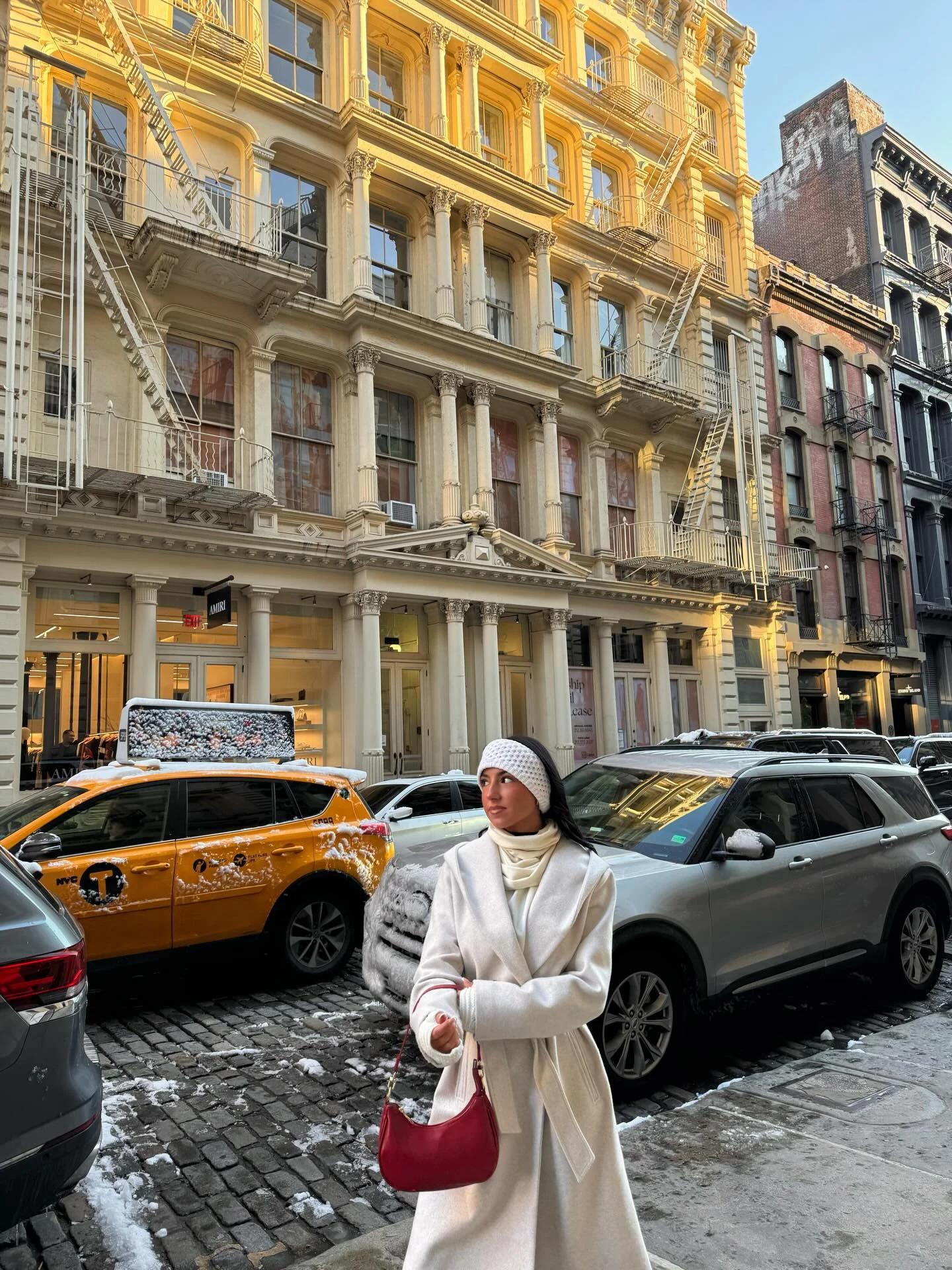 Woman in a cream wool coat, light blue jeans, white scarf, and brown ankle boots outdoors.