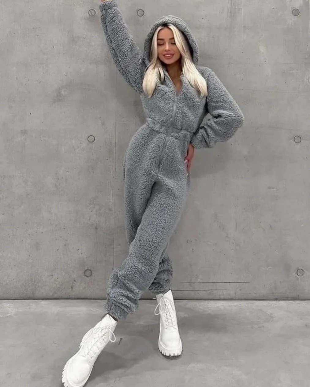 Model wearing a gray hooded zip-front jumpsuit with white chunky lace-up boots.