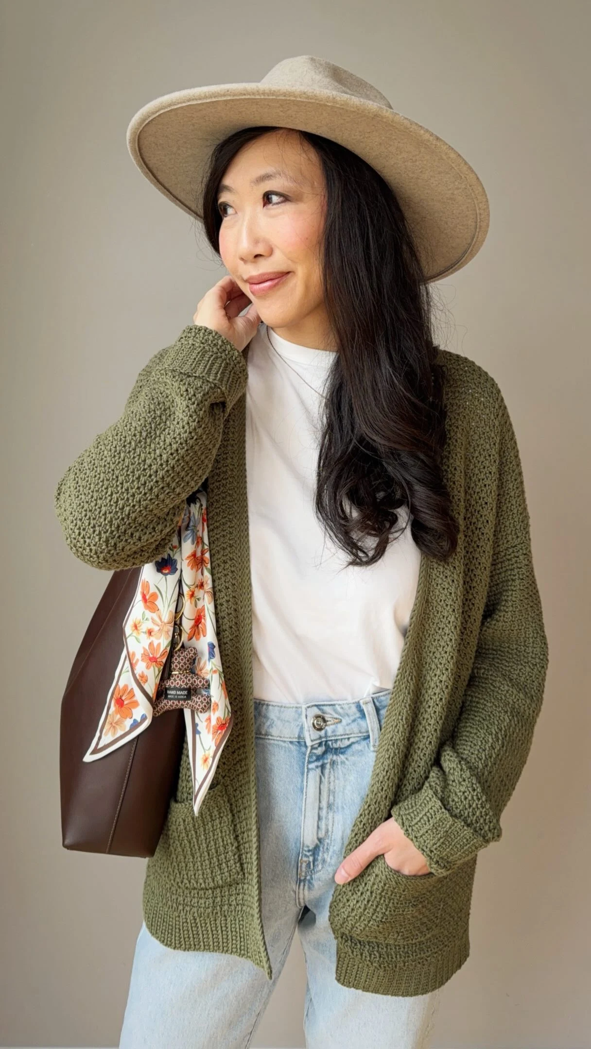Olive chunky crochet cardigan over white top and light jeans, styled with a wide-brimmed beige hat.