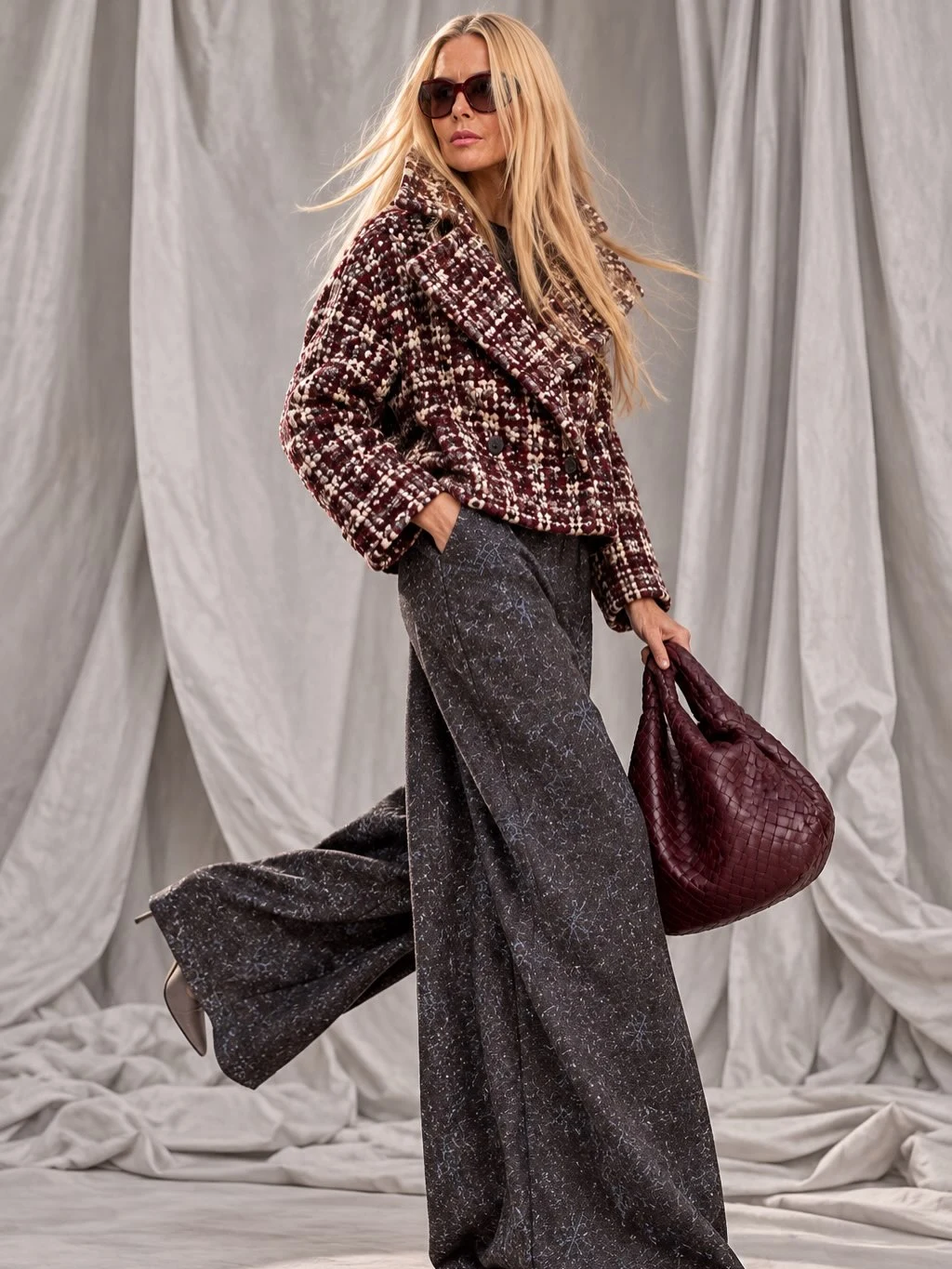 Patterned cropped double-breasted jacket with charcoal wide-leg trousers, dark sunglasses, and burgundy woven bag.