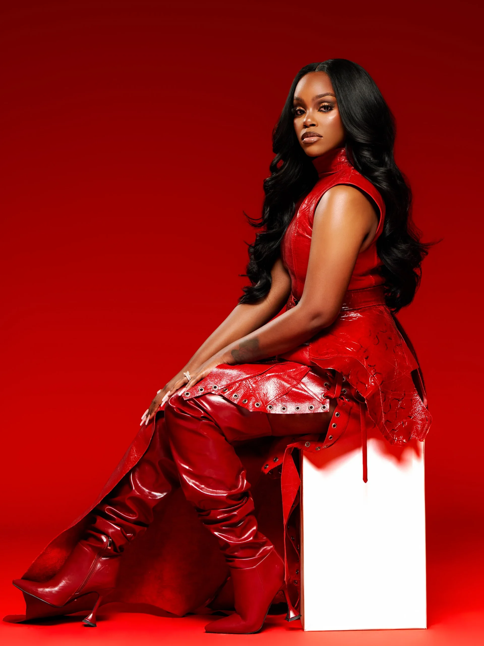 All-red outfit with a sleeveless top, glossy gathered pants, flowing train, and pointed heeled boots.