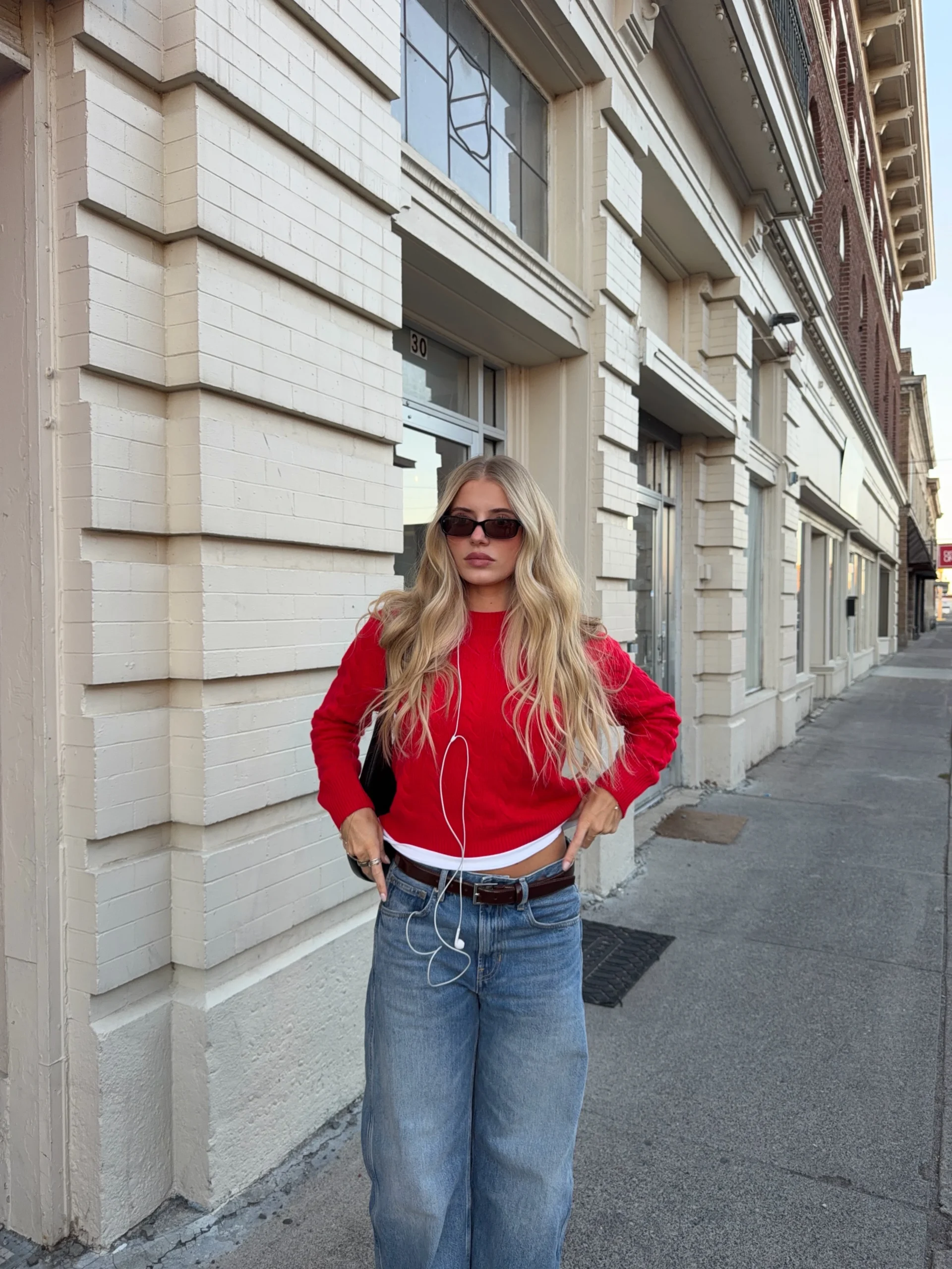 Person wearing a bright red sweater, white top, wide-leg blue jeans, brown belt, and a black shoulder bag.