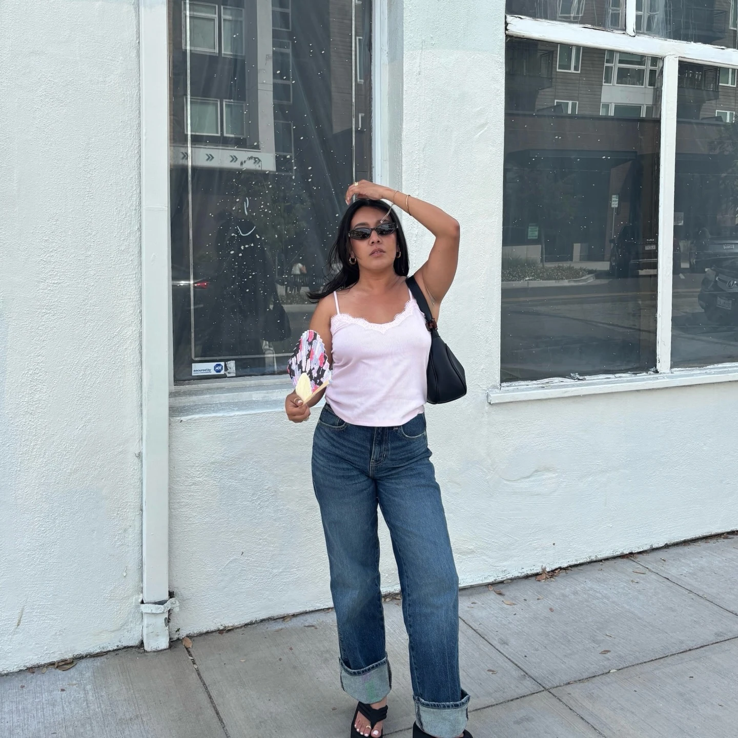 White camisole tucked into cuffed blue straight-leg jeans with black sandals and shoulder bag outdoors.