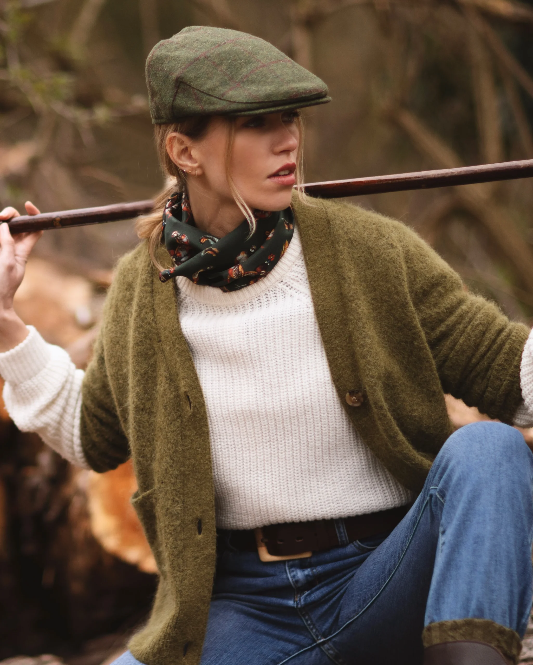 Person in a white knit sweater, olive cardigan, green tweed flat cap, and bird-print neck scarf.