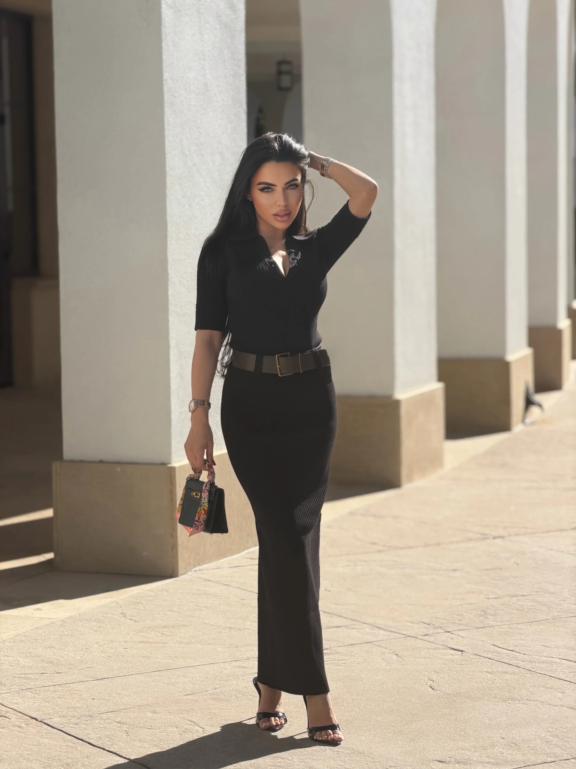 Black ribbed top and long skirt with wide belt, open-toe sandals, and colorful patterned handbag.