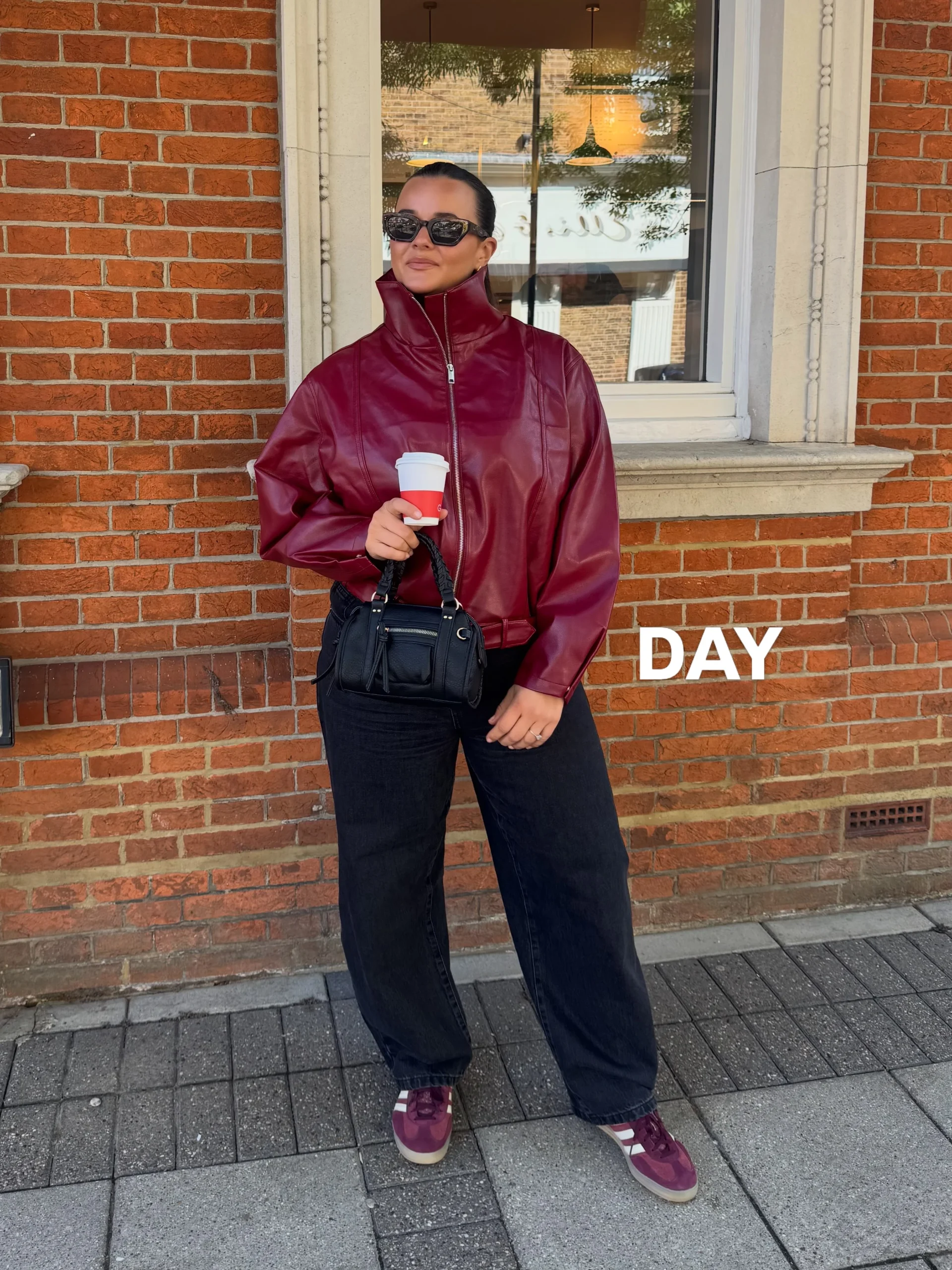 Burgundy faux-leather zip jacket worn over a black tee with dark wide-leg jeans and white sneakers.