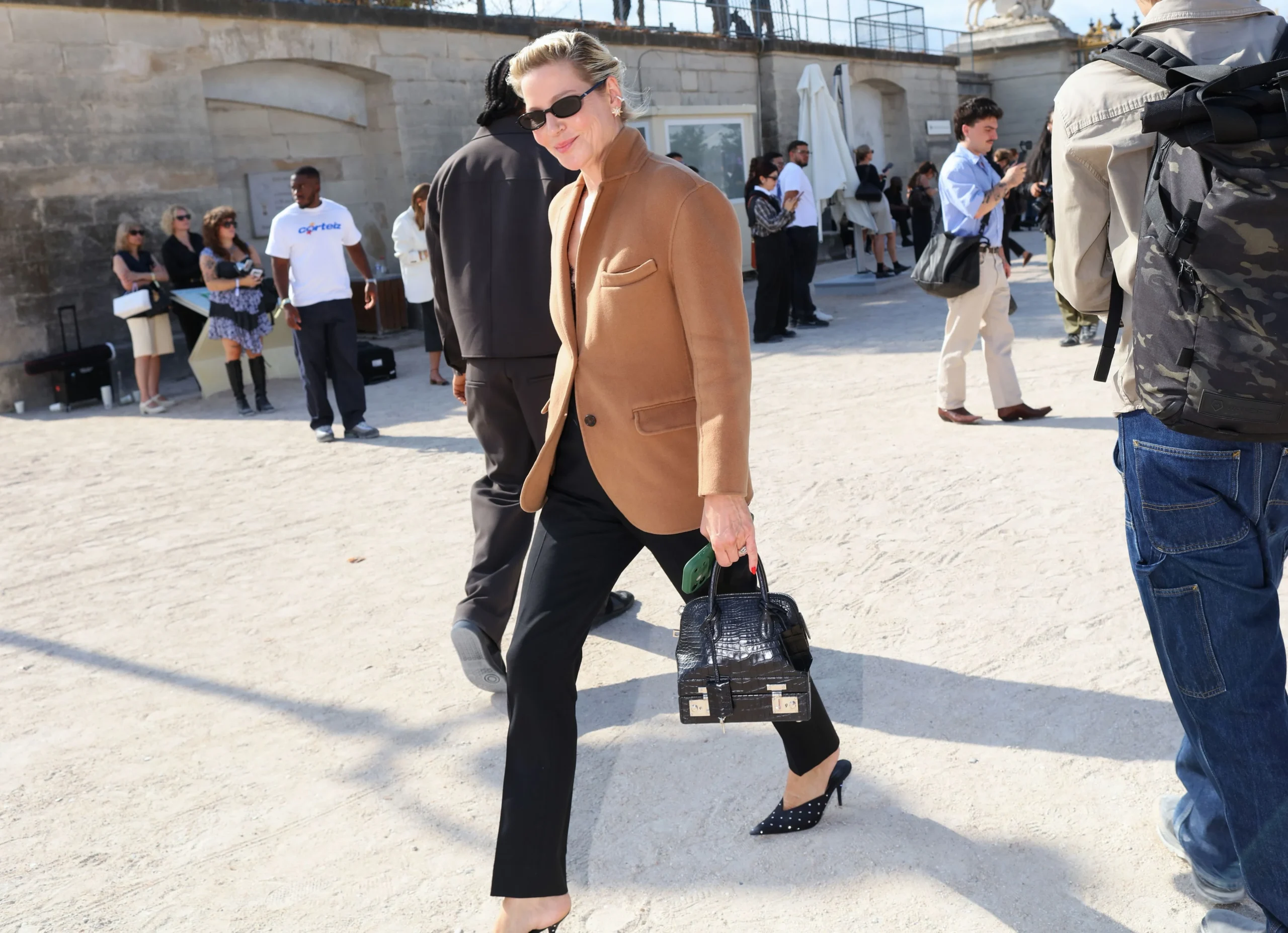 Camel blazer over black trousers and dotted pointed shoes, paired with a structured black handbag.
