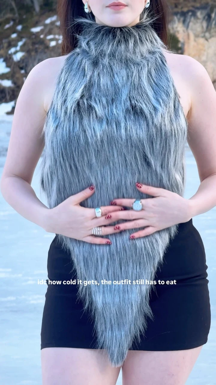 Woman wearing a grey faux-fur halter top over a black mini dress with fuzzy knee-high boot covers.