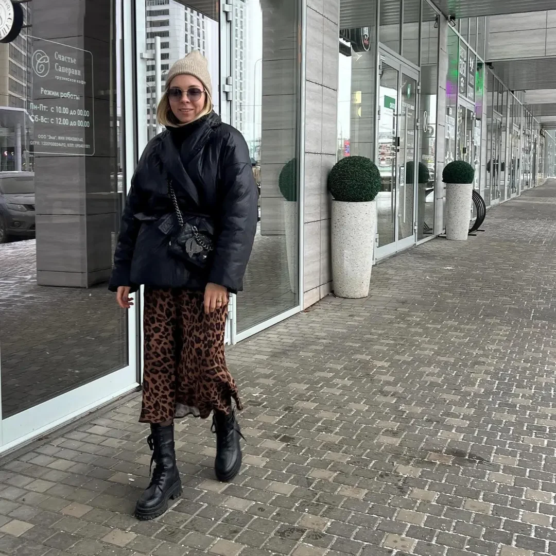 Woman wearing a long beige wool coat over a black turtleneck, straight jeans, and black ankle boots.