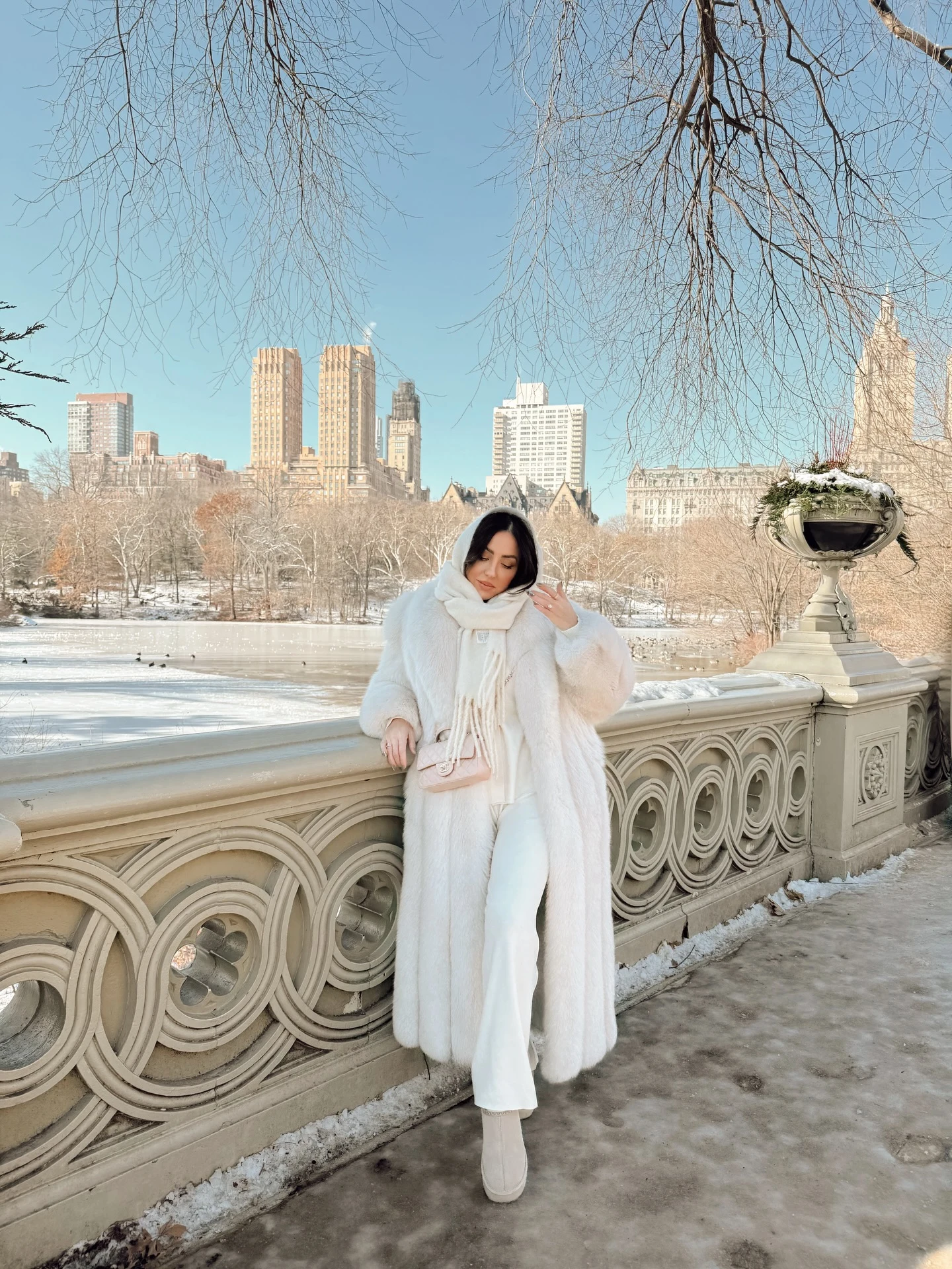 Woman dressed entirely in white wearing a long faux-fur coat, pants, boots, and beanie.