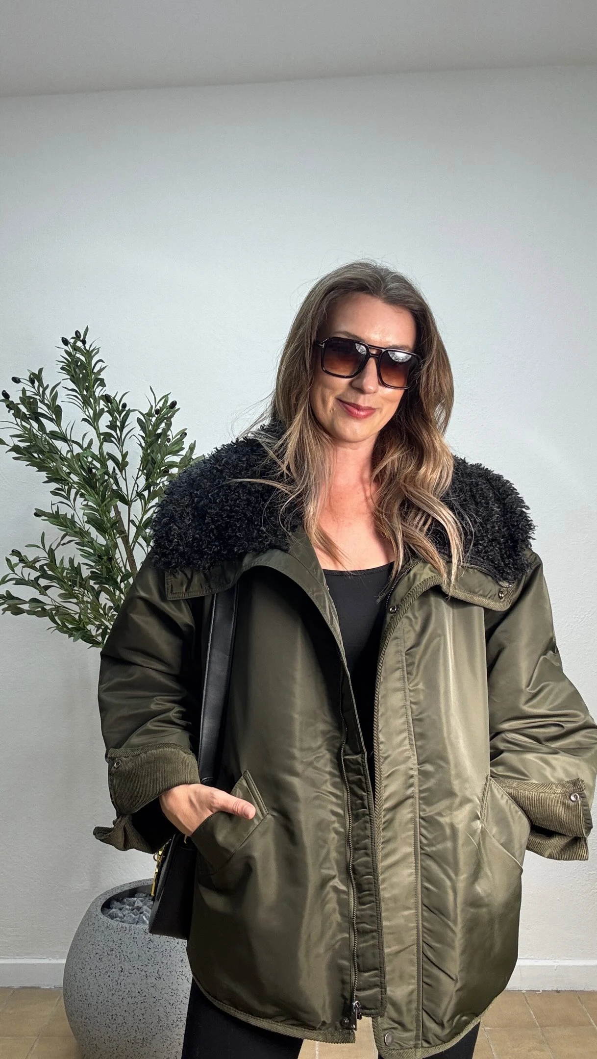 Oversized olive green jacket with black fleece collar layered over a black top and pants.