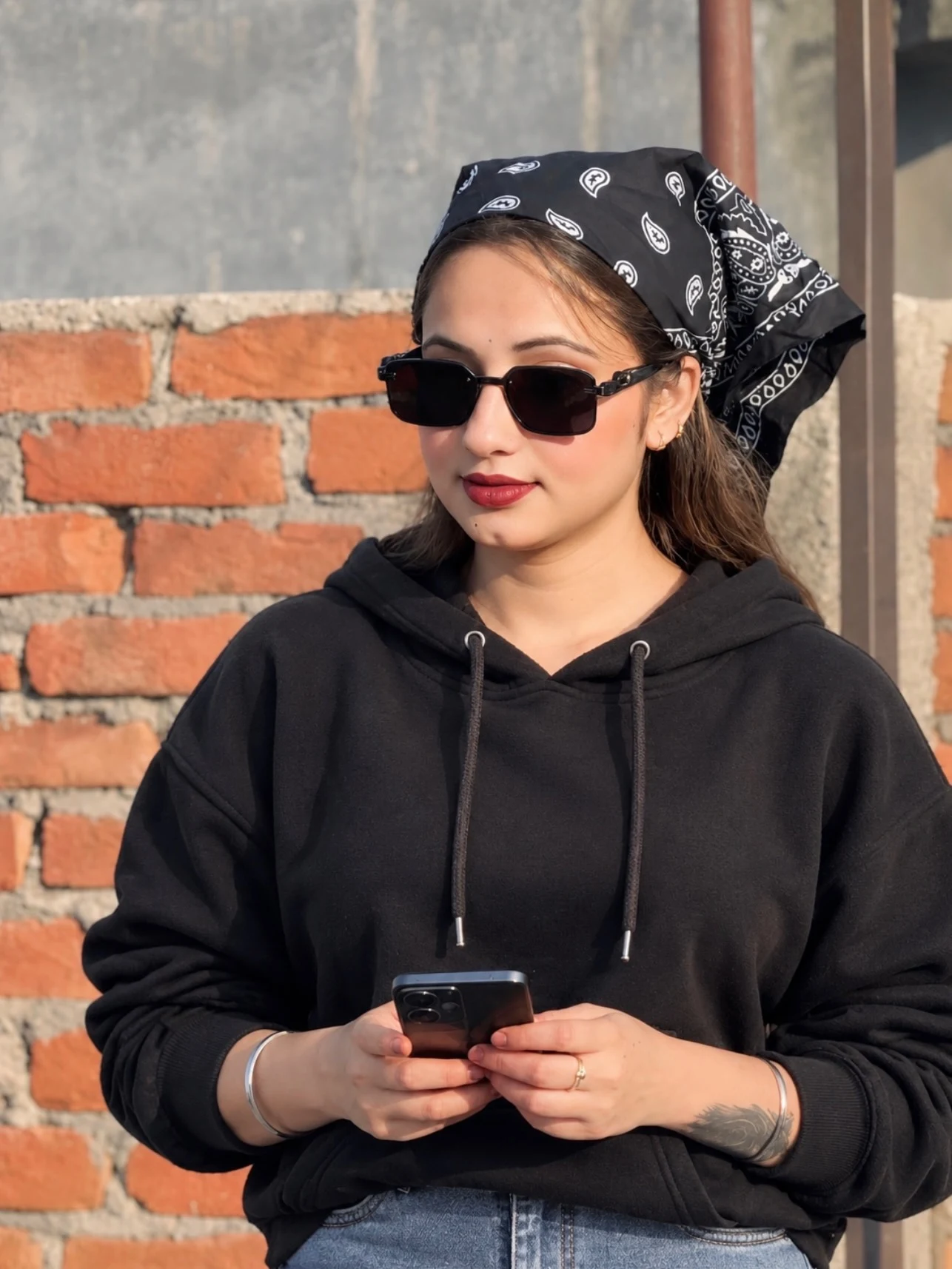 Loose black hoodie and blue jeans styled with a patterned bandana and rectangular sunglasses.