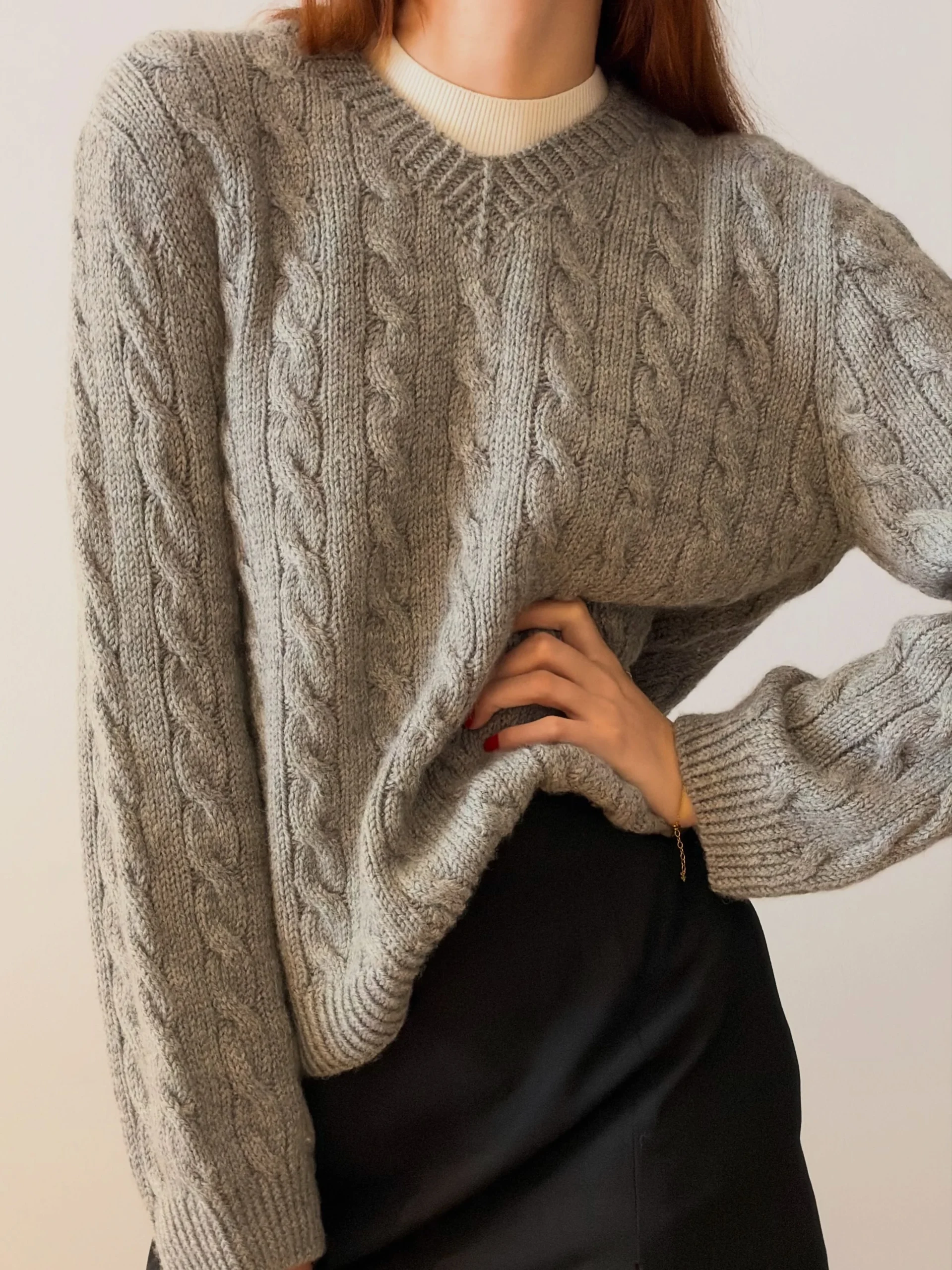 Chunky grey cable-knit sweater layered over cream turtleneck, black mini skirt with side slit, black tights