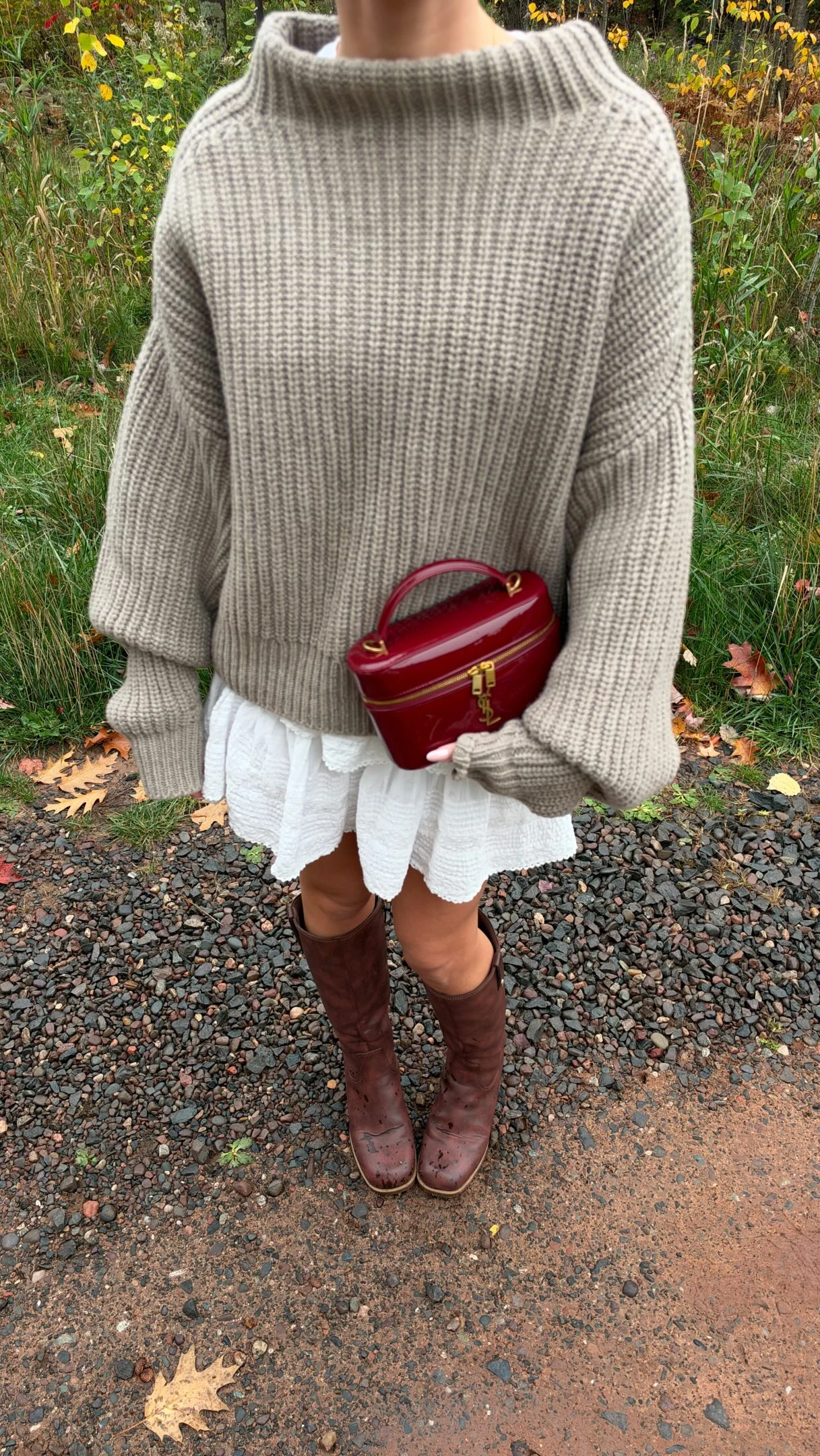 Gray ribbed sweater and white scalloped mini skirt styled with tall brown boots and a red handbag outdoors.
