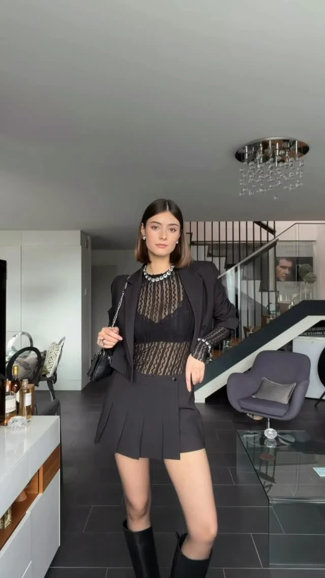 Woman in a cropped black blazer, crop top, high-waisted wide-leg trousers, and black pointed-toe boots.