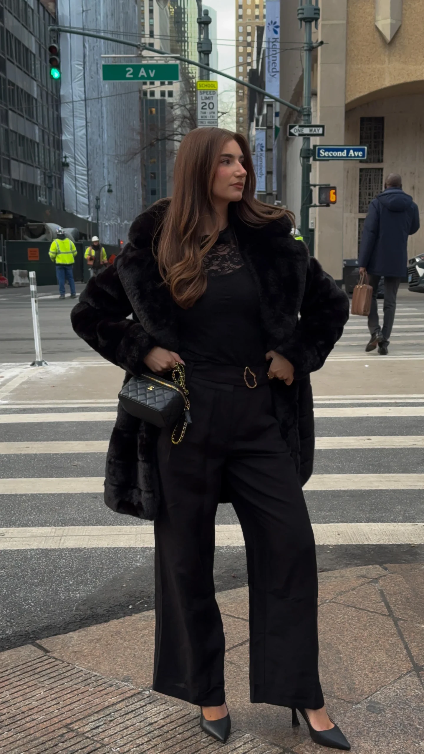 Woman in a full-length black faux-fur coat, wide-leg trousers, heels, and a quilted chain-strap bag.