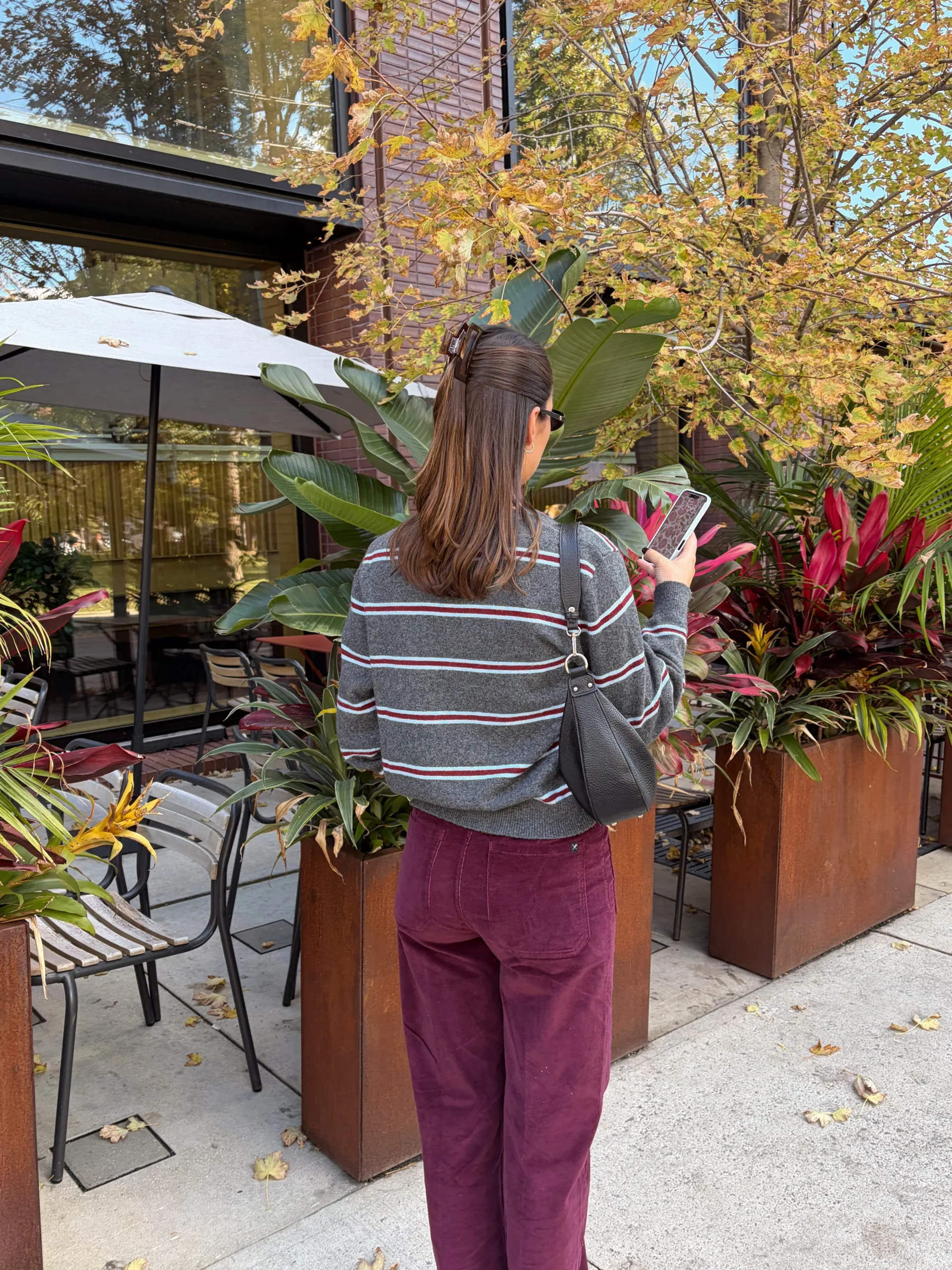 Grey striped cardigan with maroon wide-leg pants, black shoulder bag, flat shoes, and sunglasses.