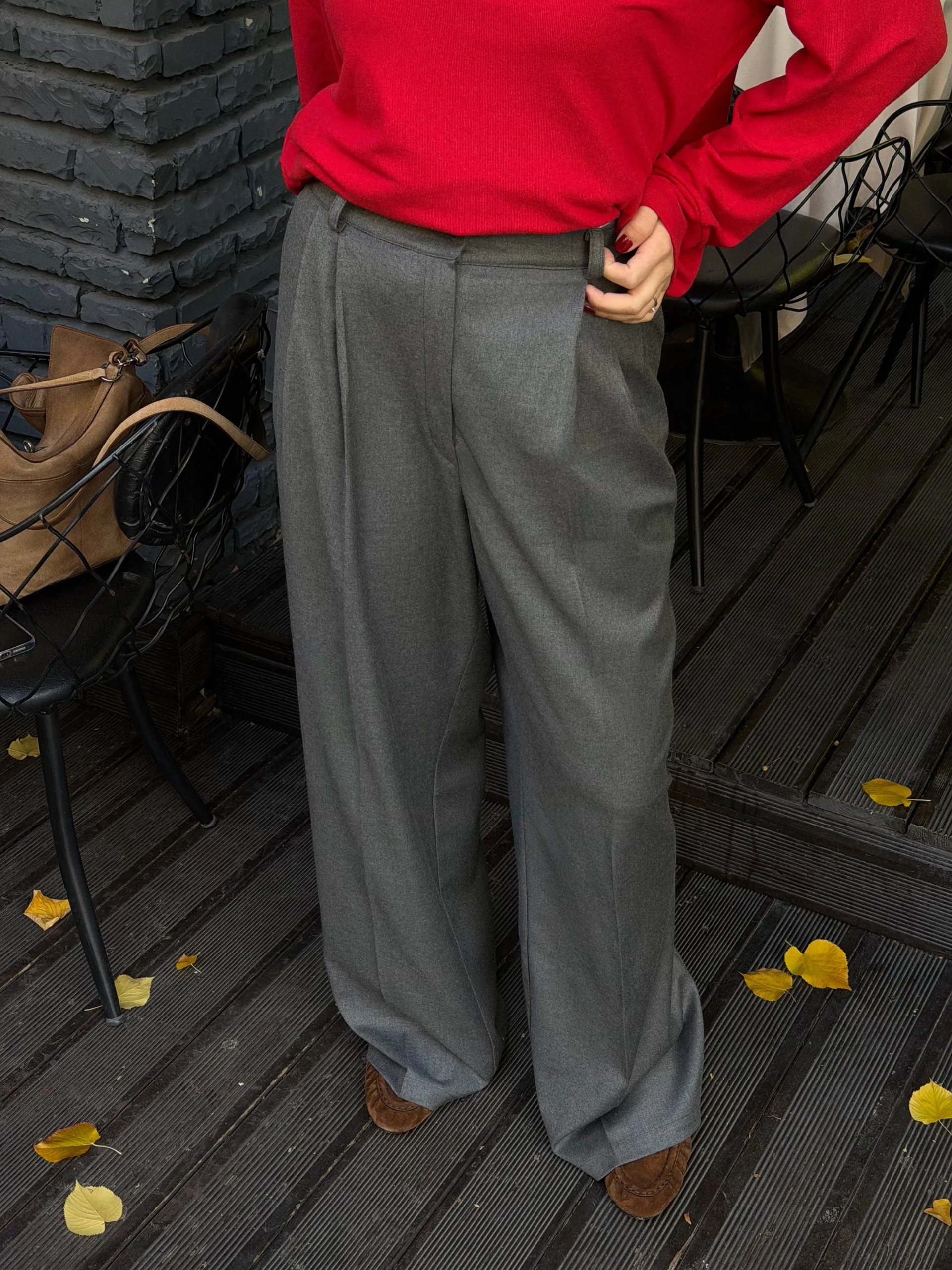 Torso-down view of a red sweater tucked into high-waisted gray pleated wide-leg trousers with brown shoes.