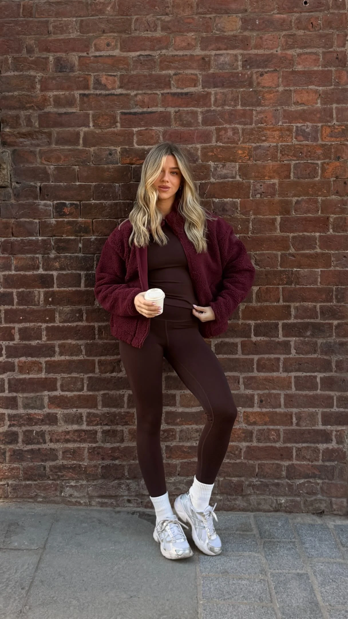 Person wearing an open burgundy zip jacket over a dark brown top and leggings with white socks and sneakers.