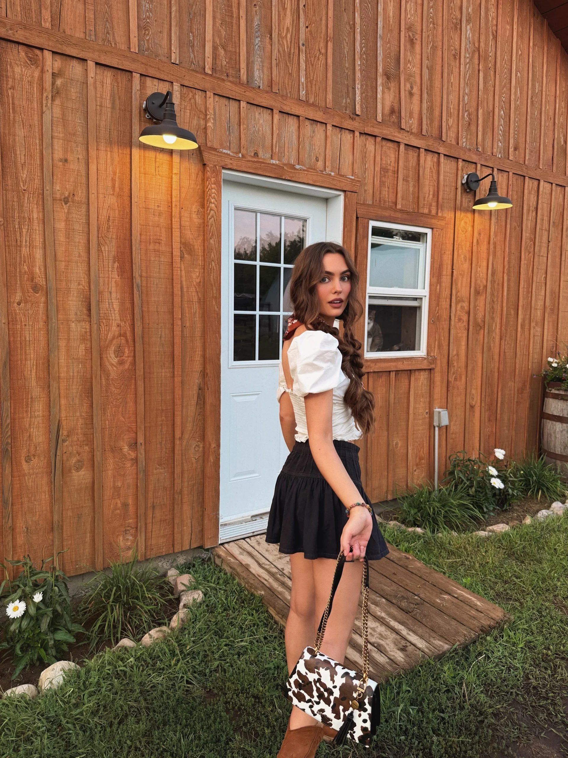 Woman wearing a white puff-sleeve crop top, black mini skirt, and brown suede cowboy boots.